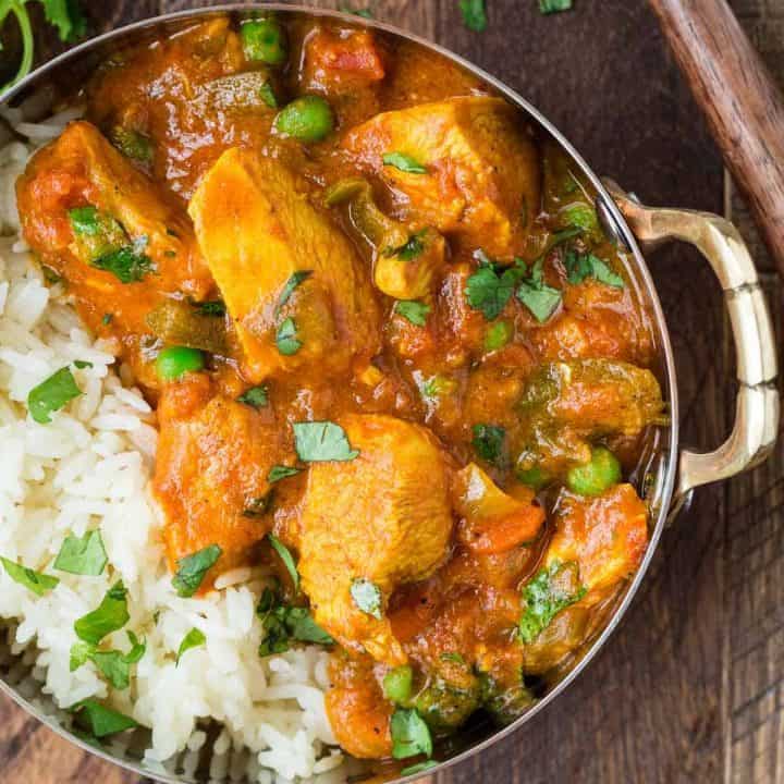 Close up of chicken served with rice, carrots, and a creamy tomato sauce. It is served in a small bowl with rice and cilantro.