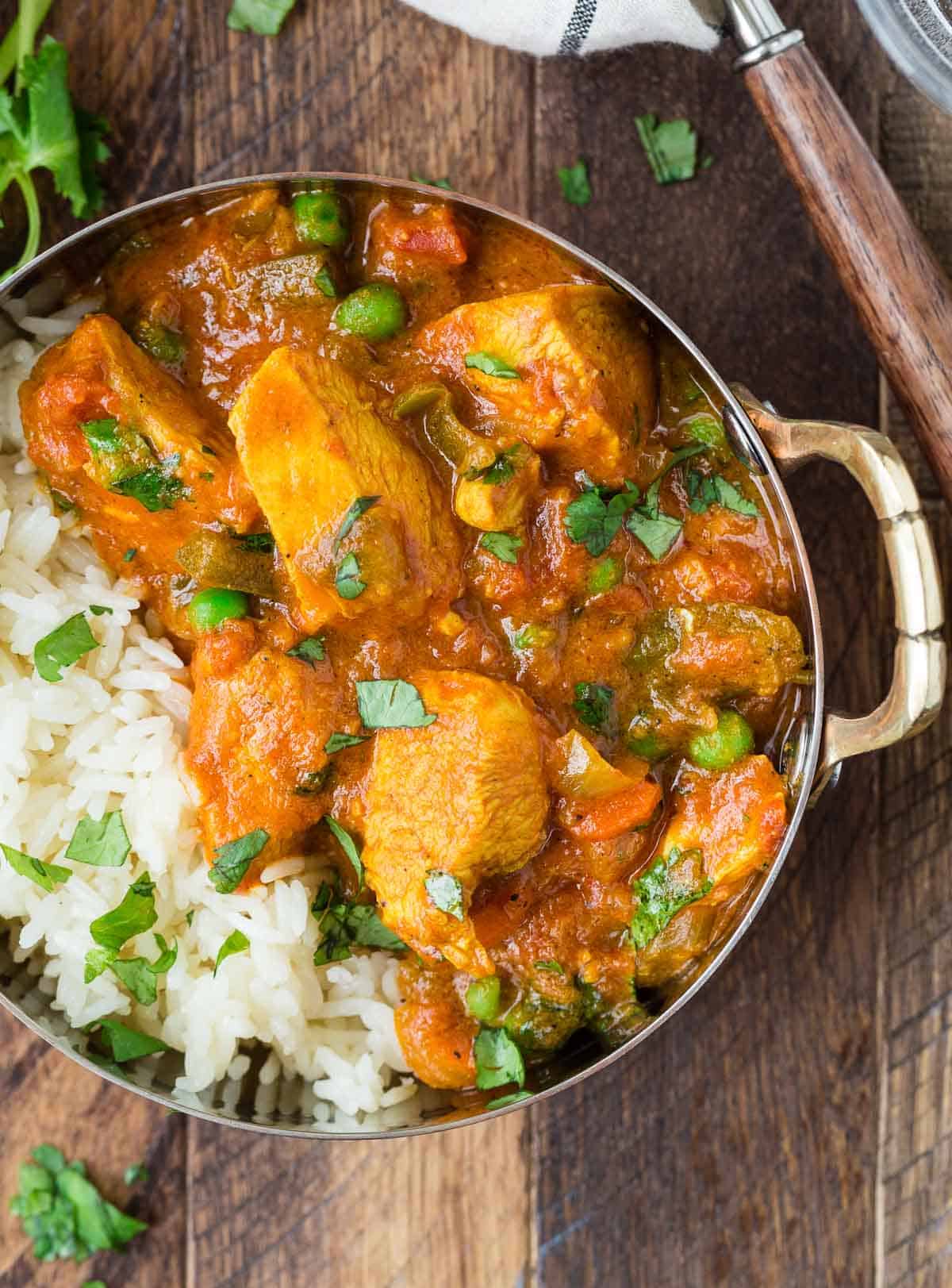 Close up of chicken served with rice, carrots, and a creamy tomato sauce. It is served in a small bowl with rice and cilantro.