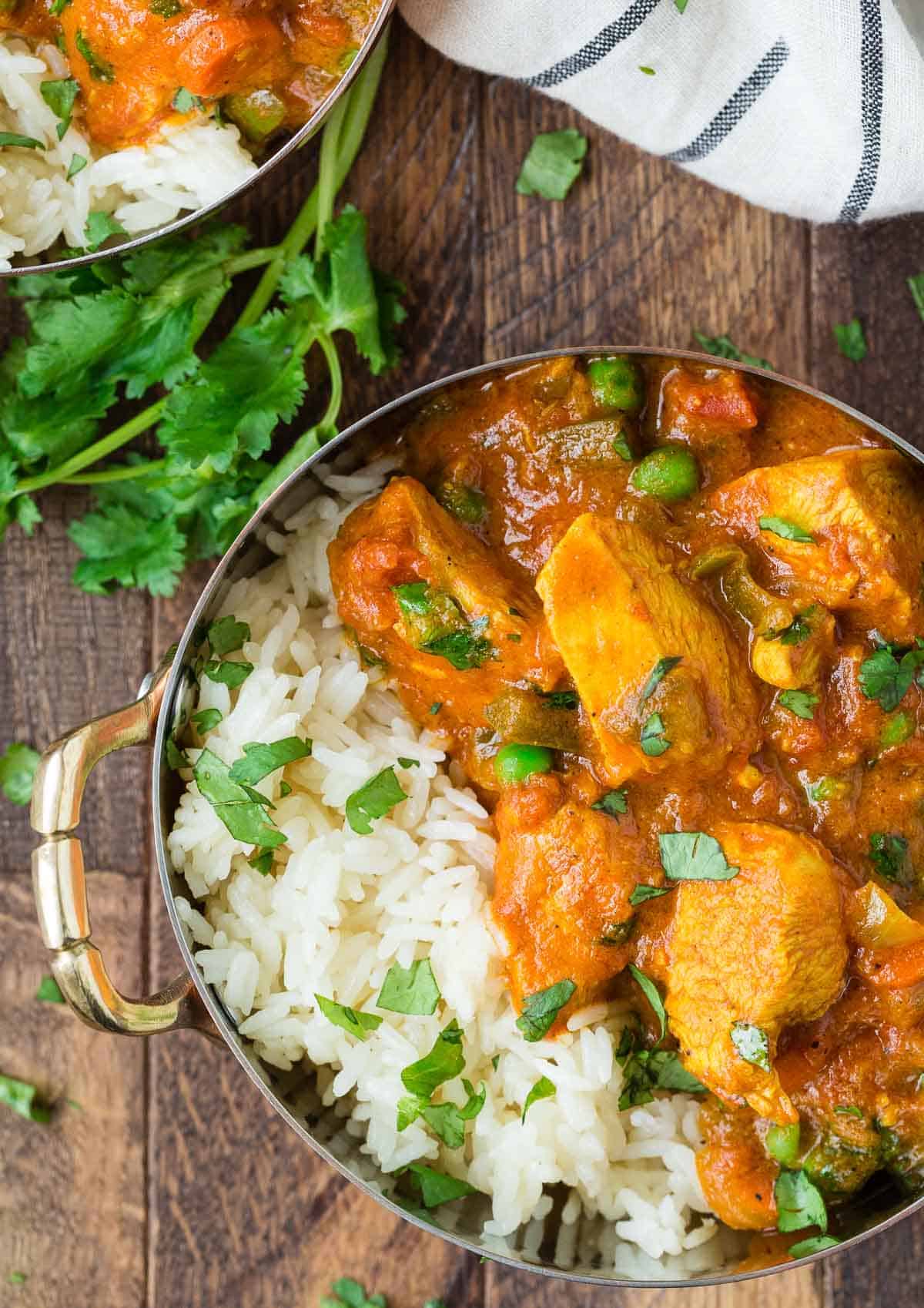 Overhead view of chicken tikka masala in a copper crock with rice and cilantro.