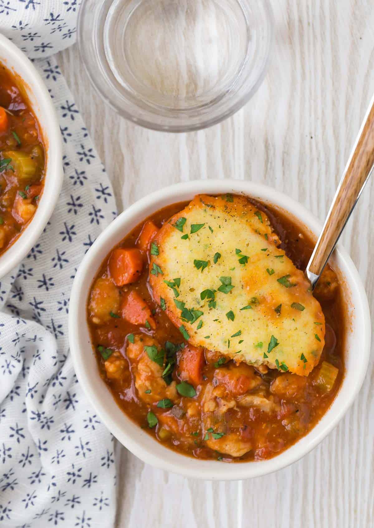 Tomato based chicken and dumplings made with cornmeal dumplings, in a small bowl.