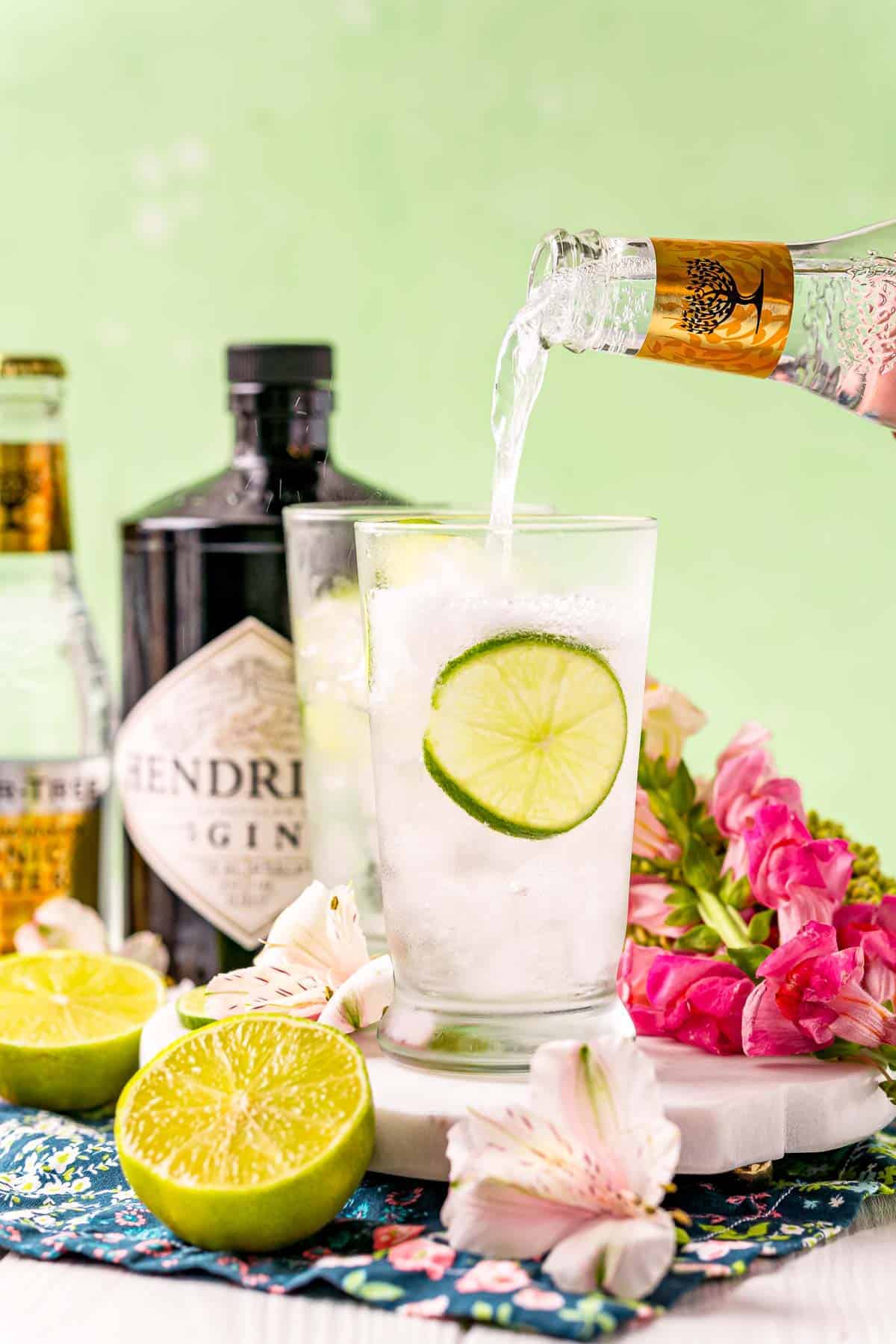 Tonic water being poured into a glass with ice and lime.