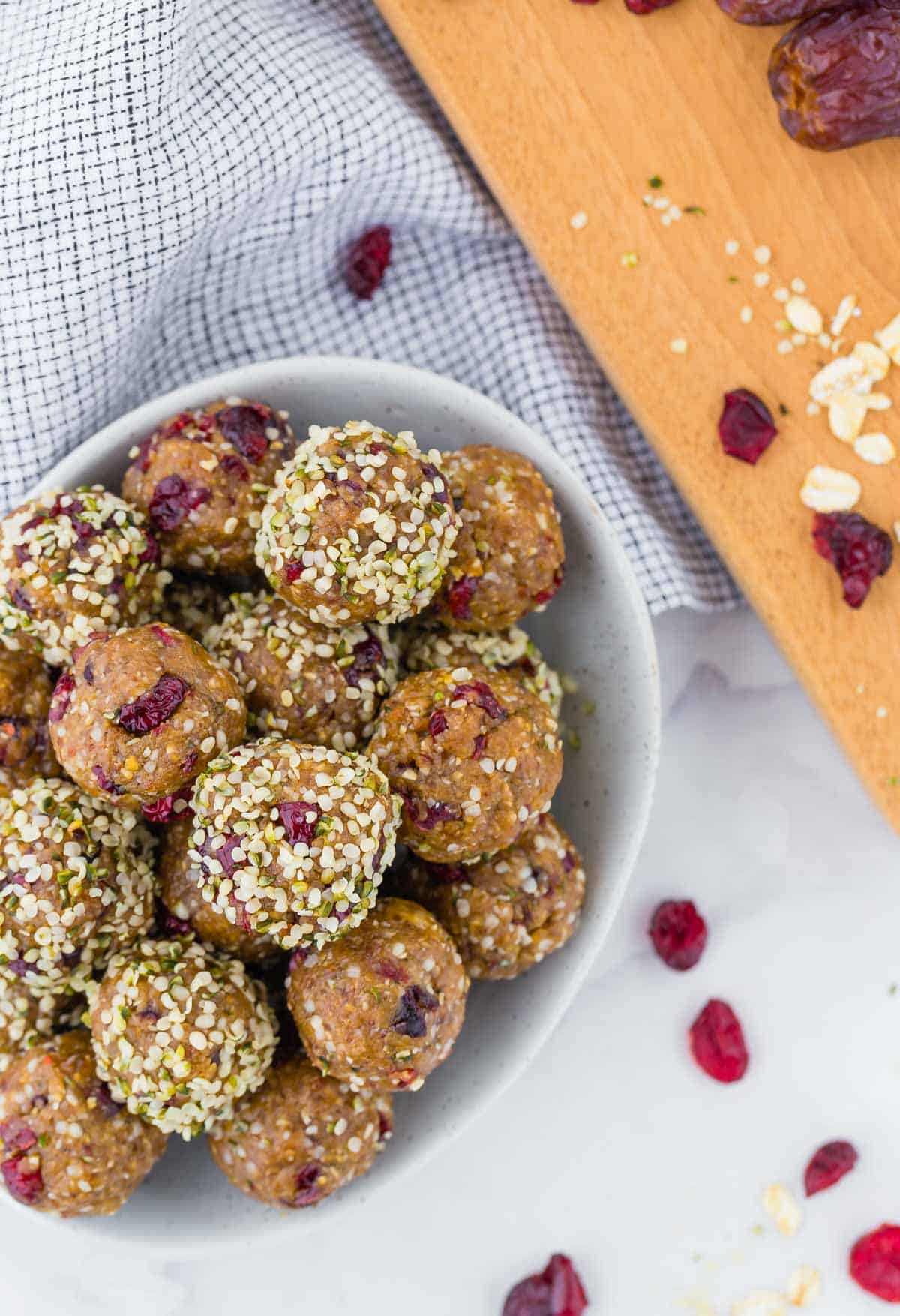 Overhead view of bowl of energy bites, with dried cranberries, oats and hemp seeds also pictured.