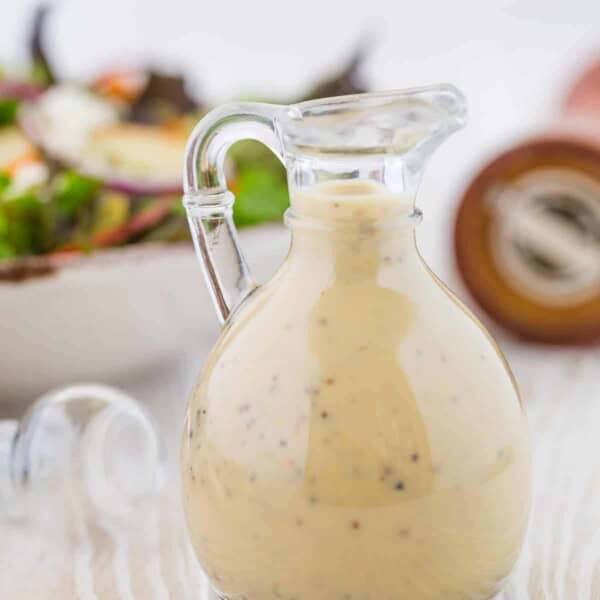 Small glass bottle of creamy maple dressing, a pepper cracker in the background.