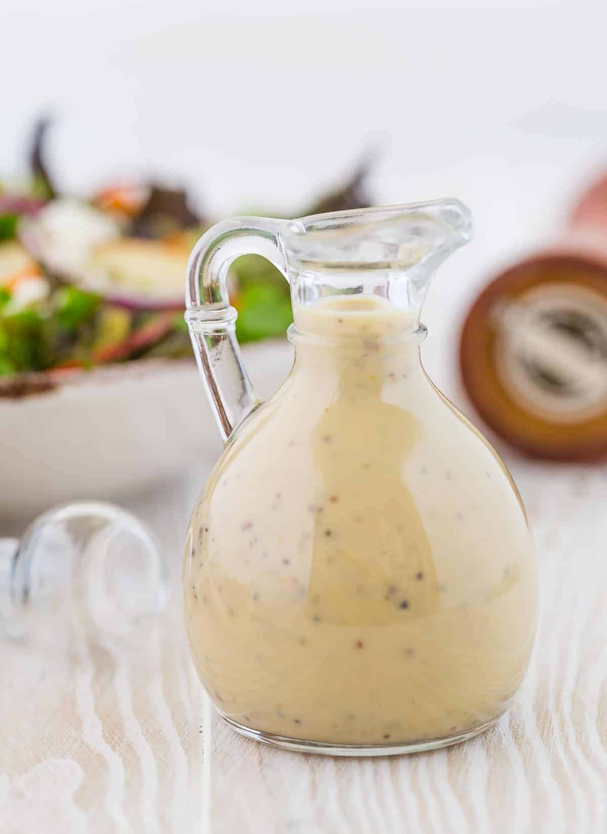 Small glass bottle of creamy maple dressing, a pepper cracker in the background.