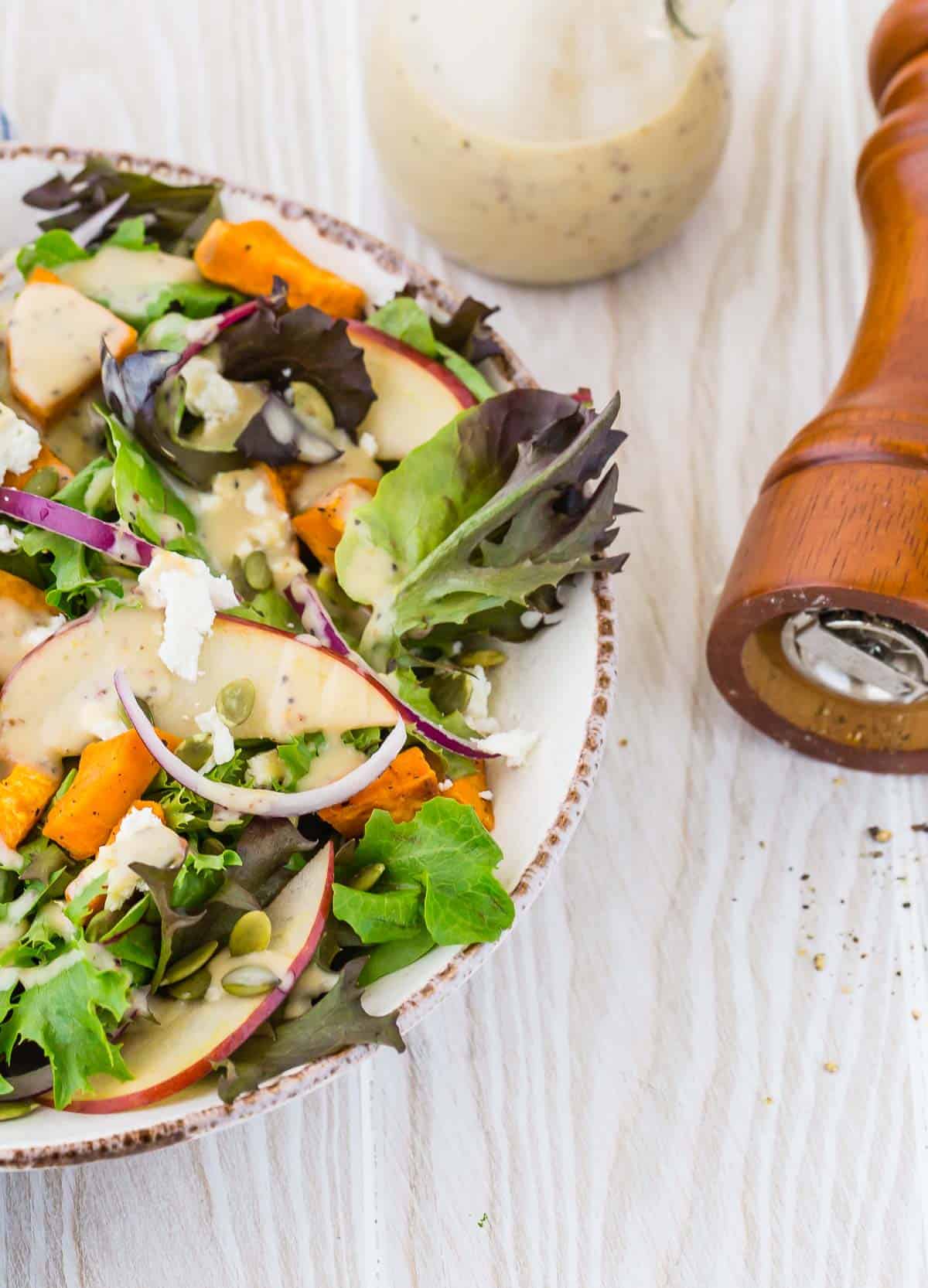 Colorful fall salad with dressing, a tipped over pepper mill also pictured.