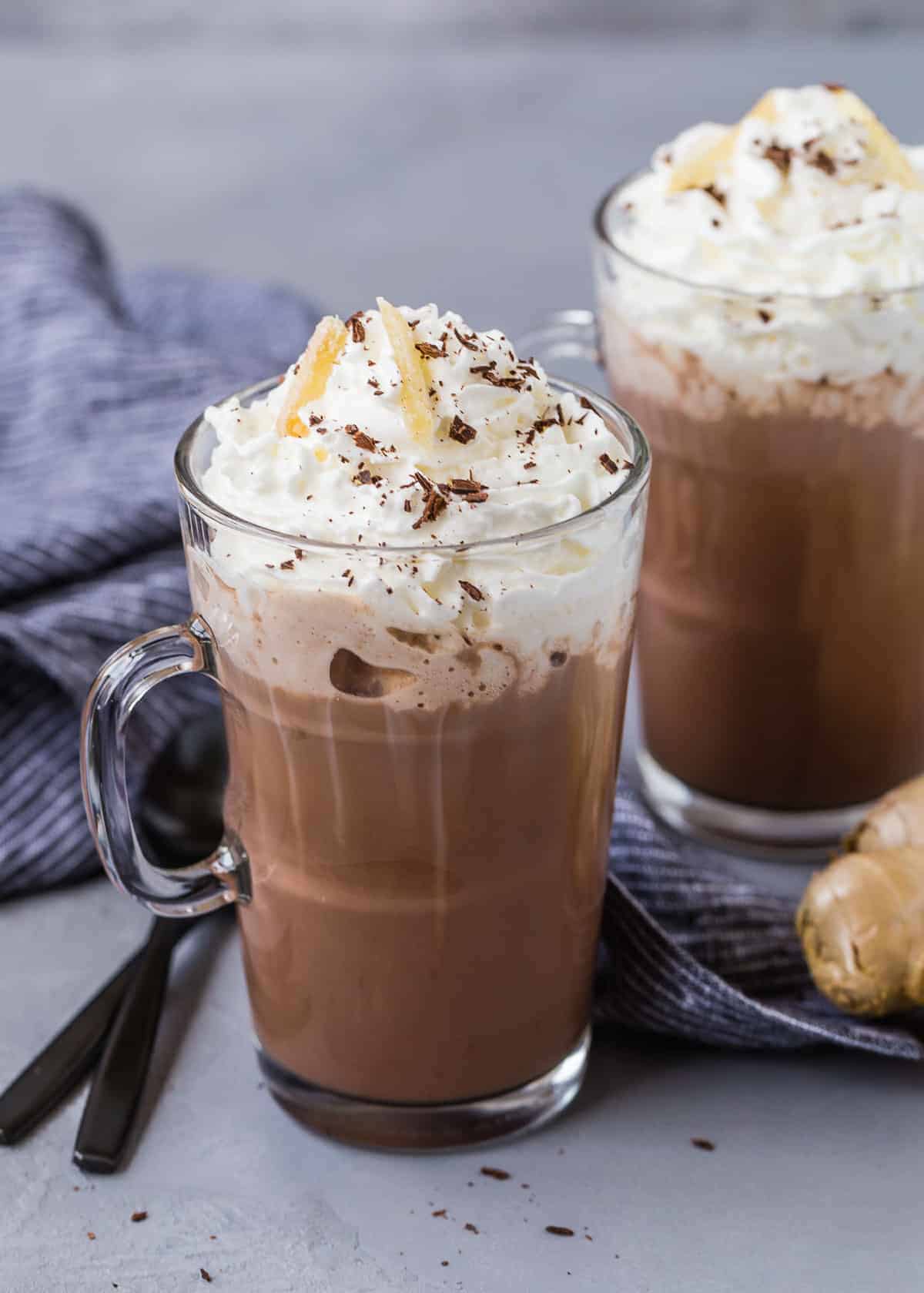 Hot cocoa in mugs, two black spoons, and a nob of fresh ginger.