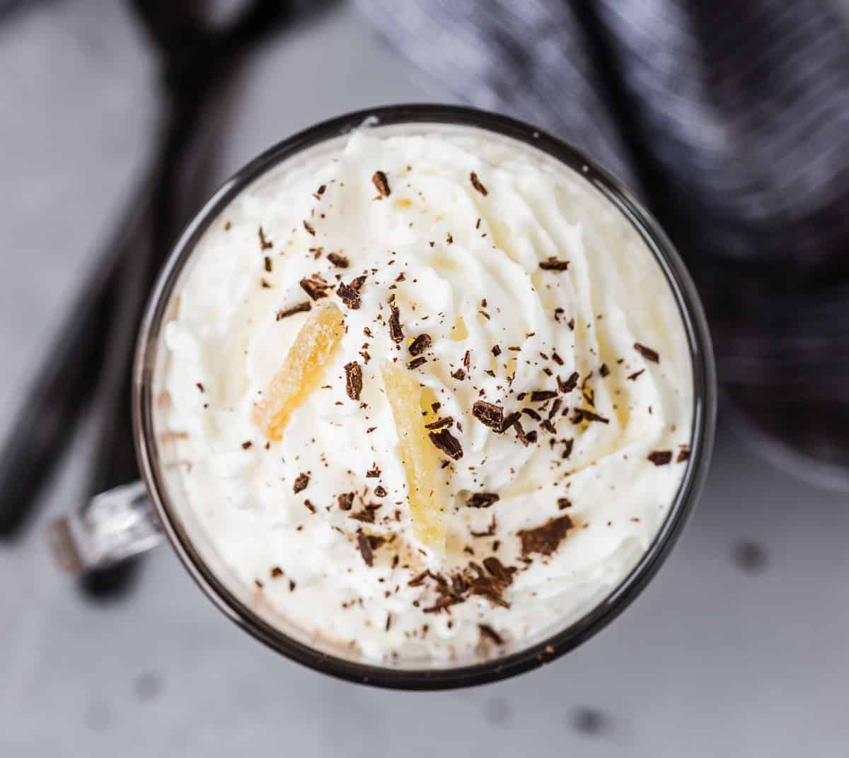 Overhead view of whipped cream topped cocoa, garnished with chocolate shavings and candied ginger.