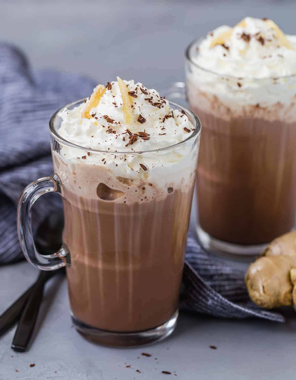 Two mugs of microwave hot chocolate topped with whipped cream, chocolate shavings, and candied ginger.