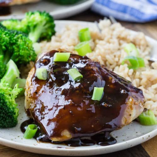 Honey balsamic chicken thigh on a plate with rice and broccoli, garnished with green onions.