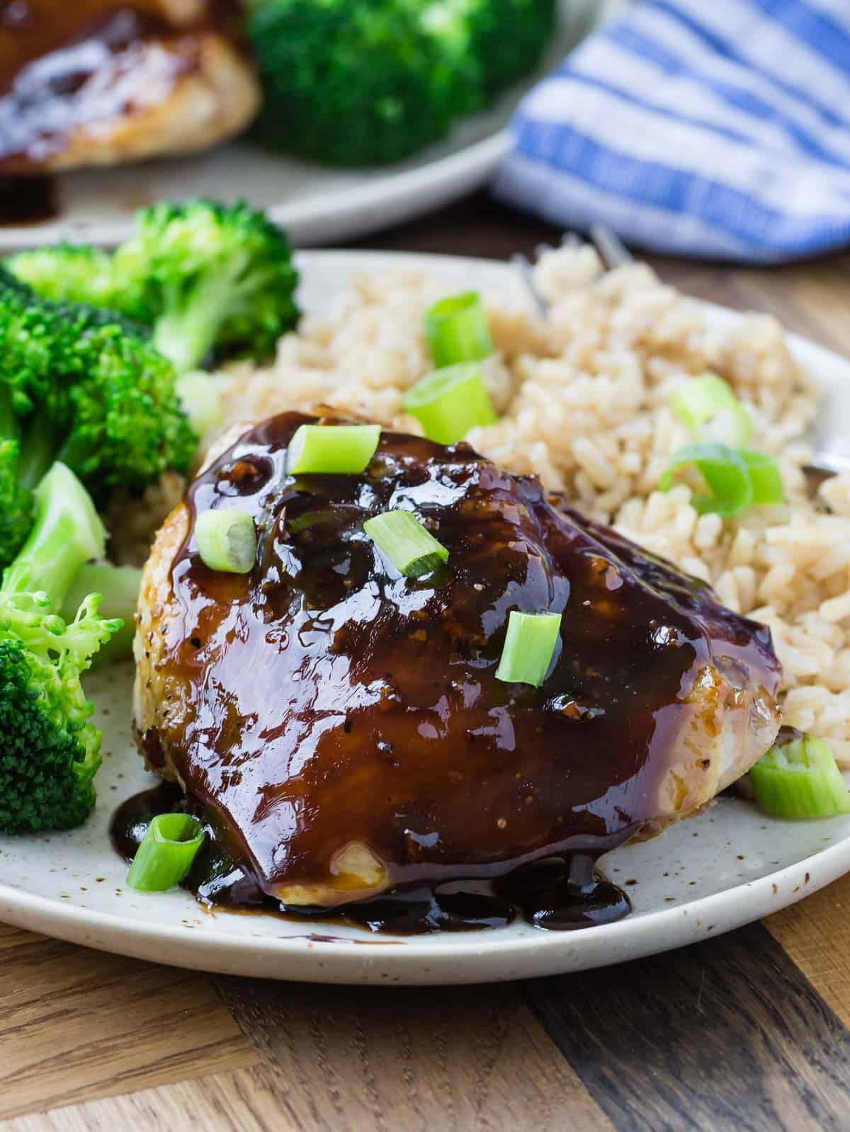 Honey balsamic chicken thigh on a plate with rice and broccoli, garnished with green onions. 