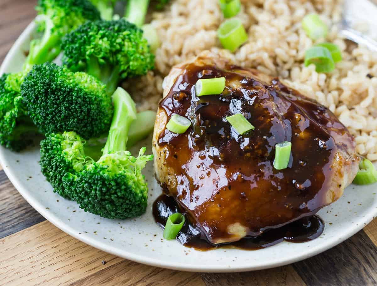 Chicken high with shiny glaze on a plate with broccoli.