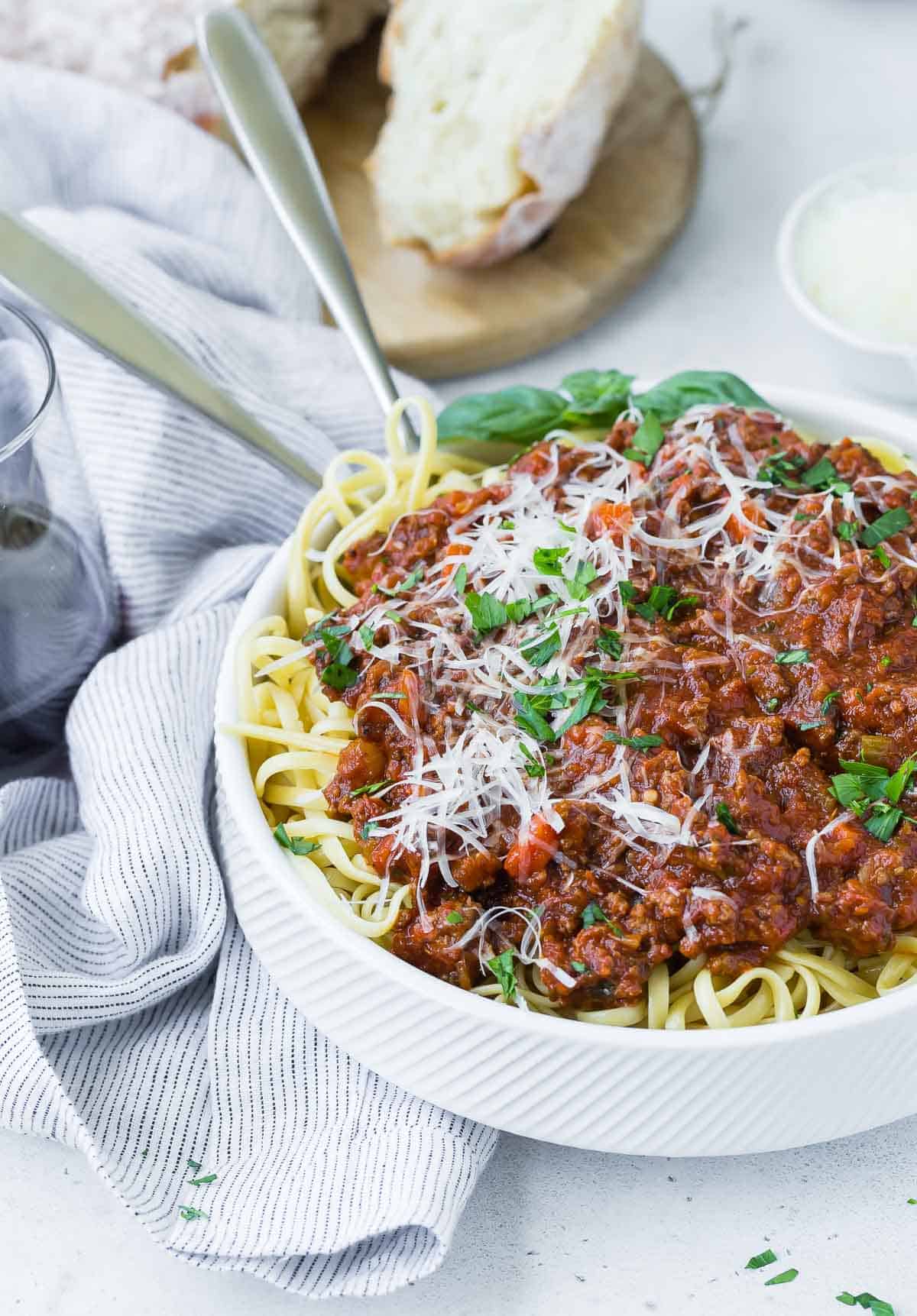 Spaghetti and Bolognese sauce in a white bowl, bread in background.