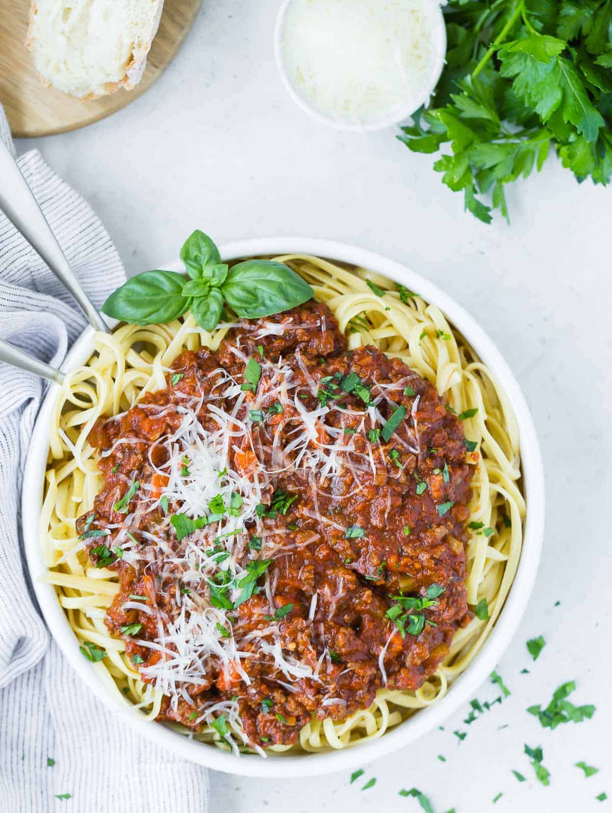 Overhead view of spaghetti and instant pot bolognese sauce in a white bowl, garnished with cheese and fresh basil.