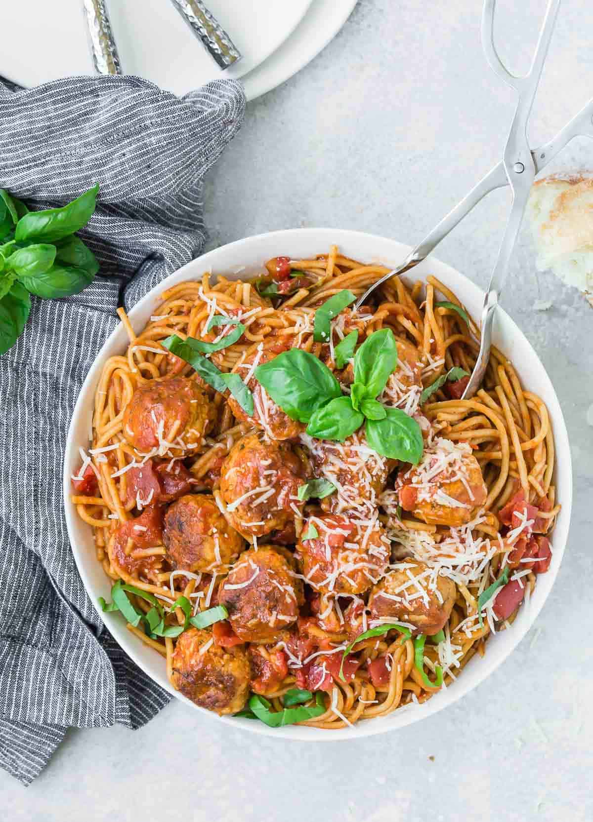 Overhead view of a white bowl with spaghetti, meatballs, and a tomato sauce.