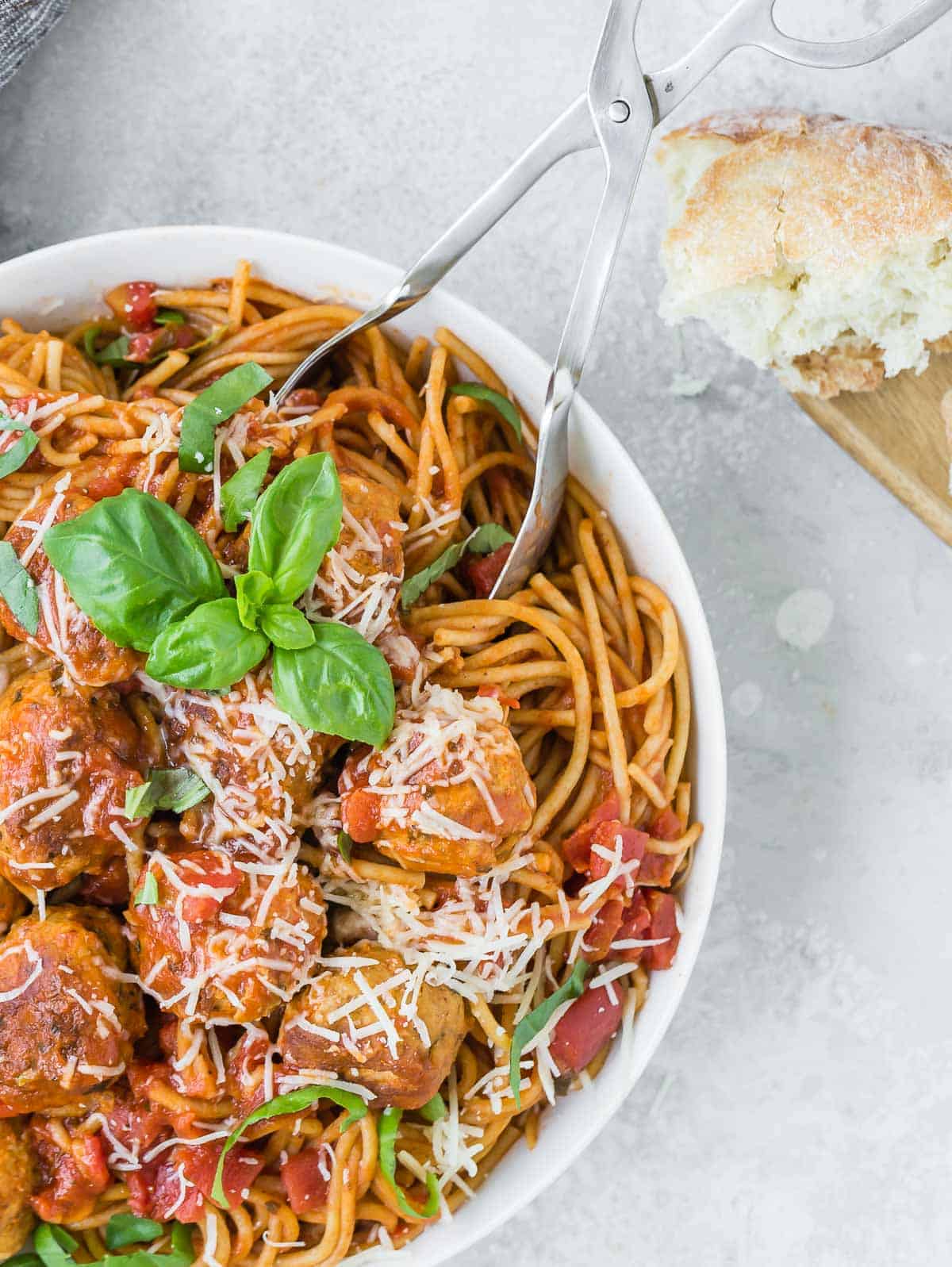 Large white bow of spaghetti and meatballs, garnished with cheese and fresh basil.