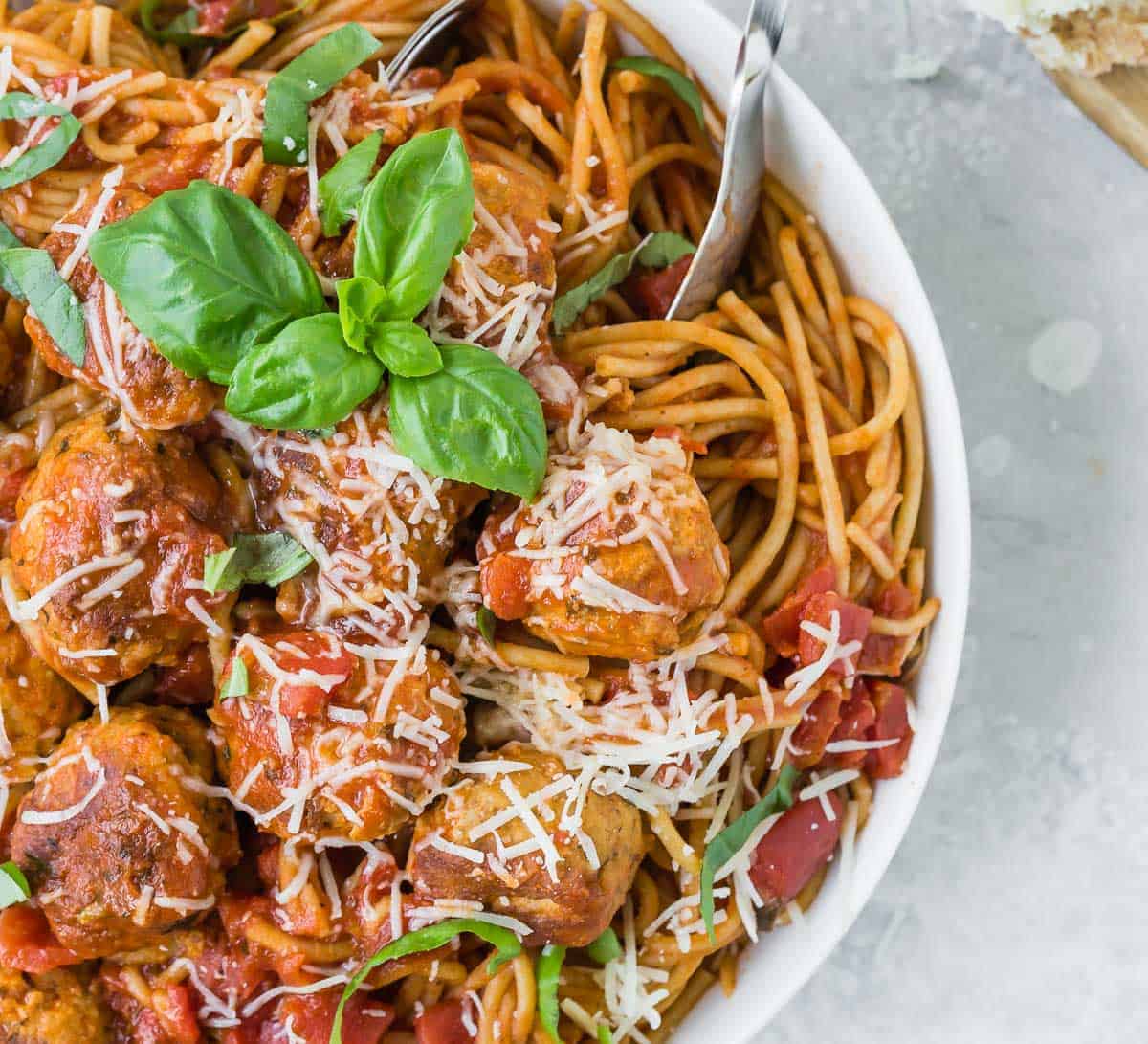 Close up overhead view of spaghetti and meatballs in a while bowl with fresh basil.