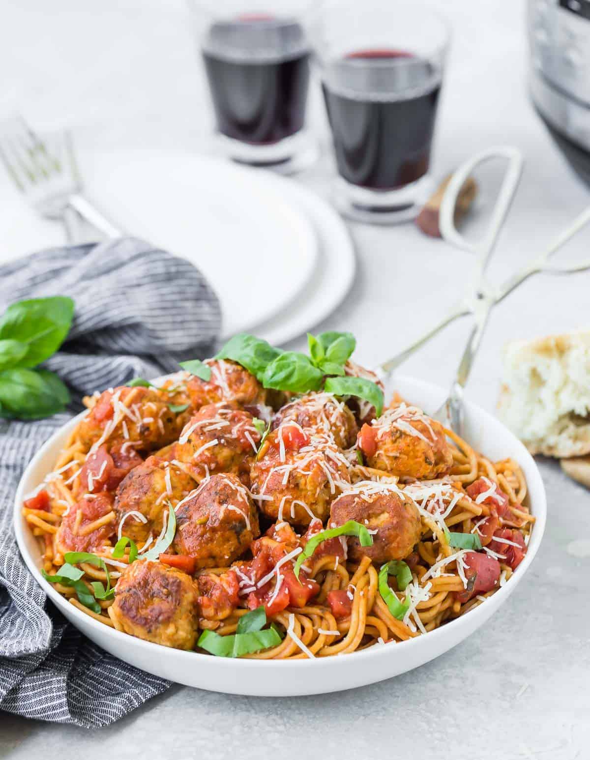 Spaghetti and meatballs with two glasses of wine in the backgorund.