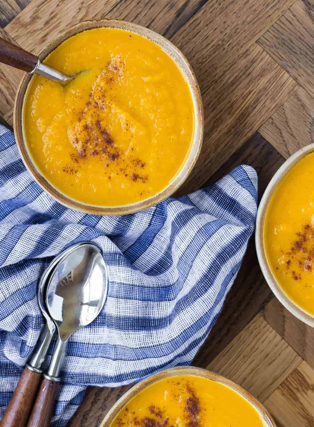 Overhead view of three bowls of squash soup made with kabocha squash. Two bowls are only partially visible.