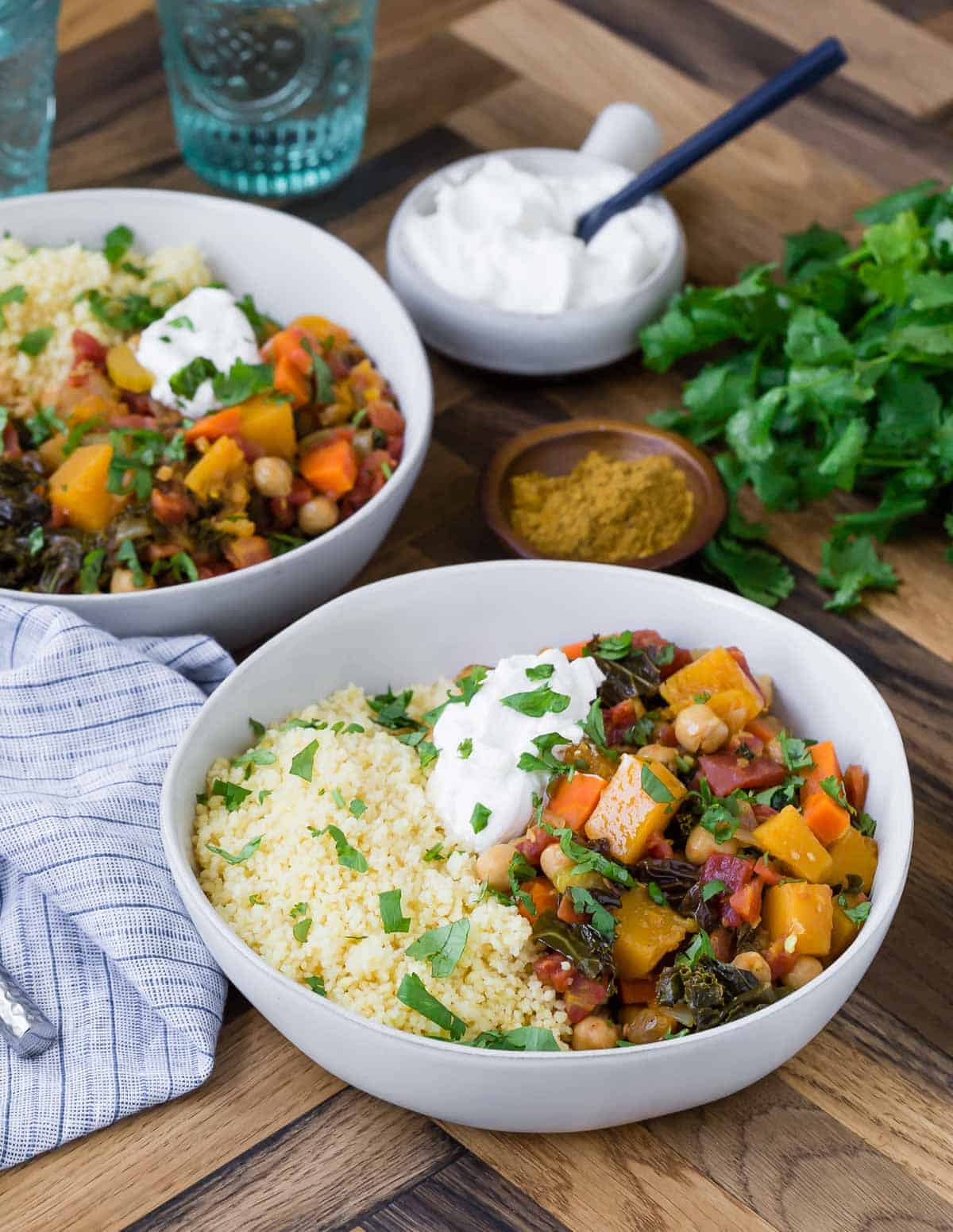 Two bowls of hearty vegetarian stew served over couscous and garnished with greek yogurt.