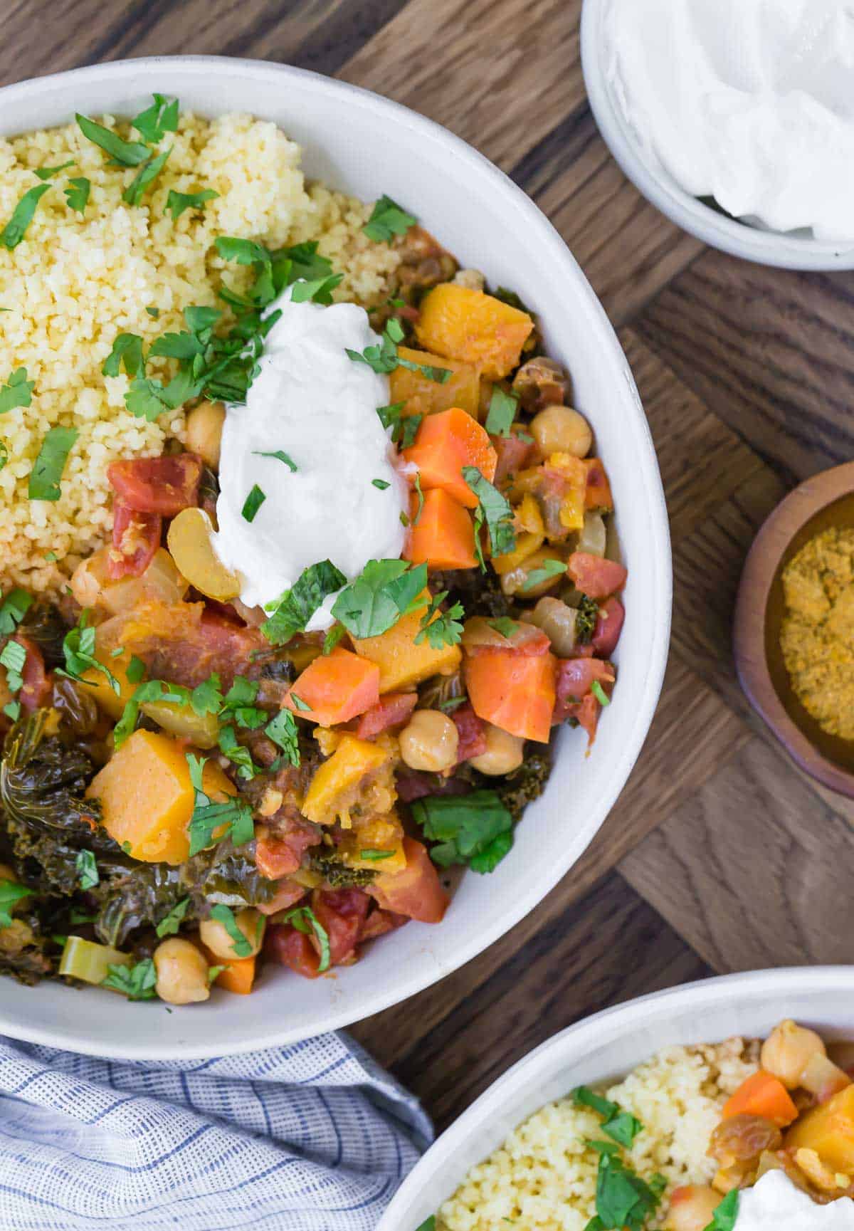 Overhead view of moroccan stew with butternut squash and chickpeas in a white bowl. It is served with yogurt and couscous.