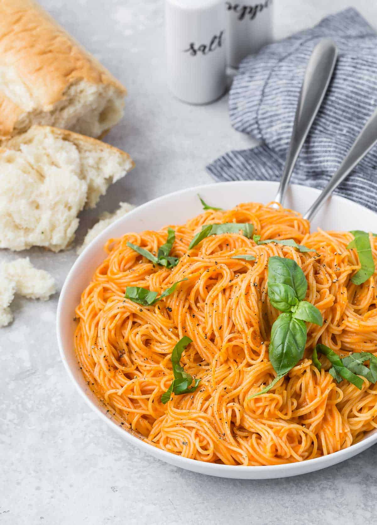 A bowl of pasta with sauce, bread in the background. Light grey background.