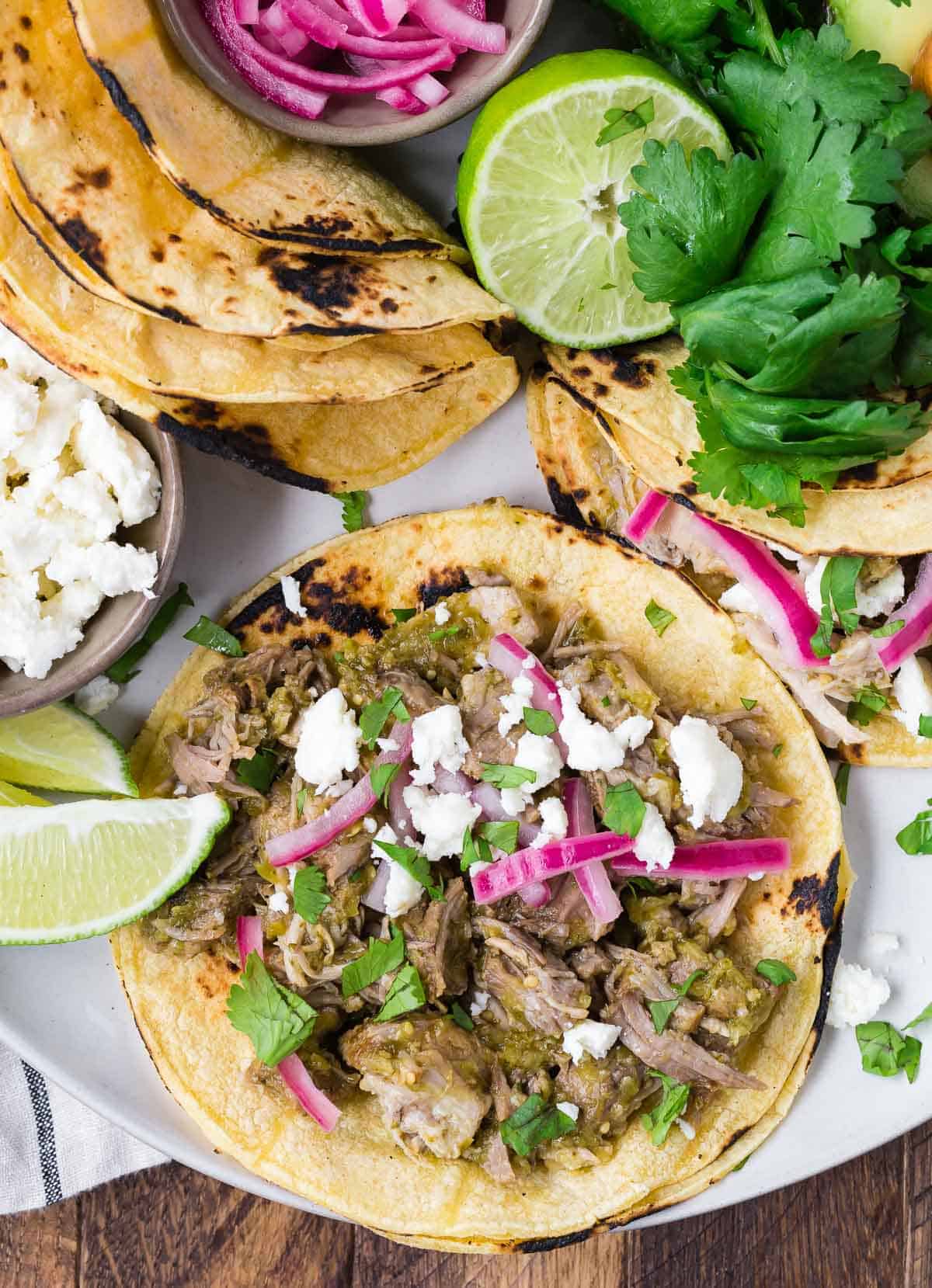 Overhead view of an open taco filled with pork, cilantro, queso fresco, and pickled red onions.