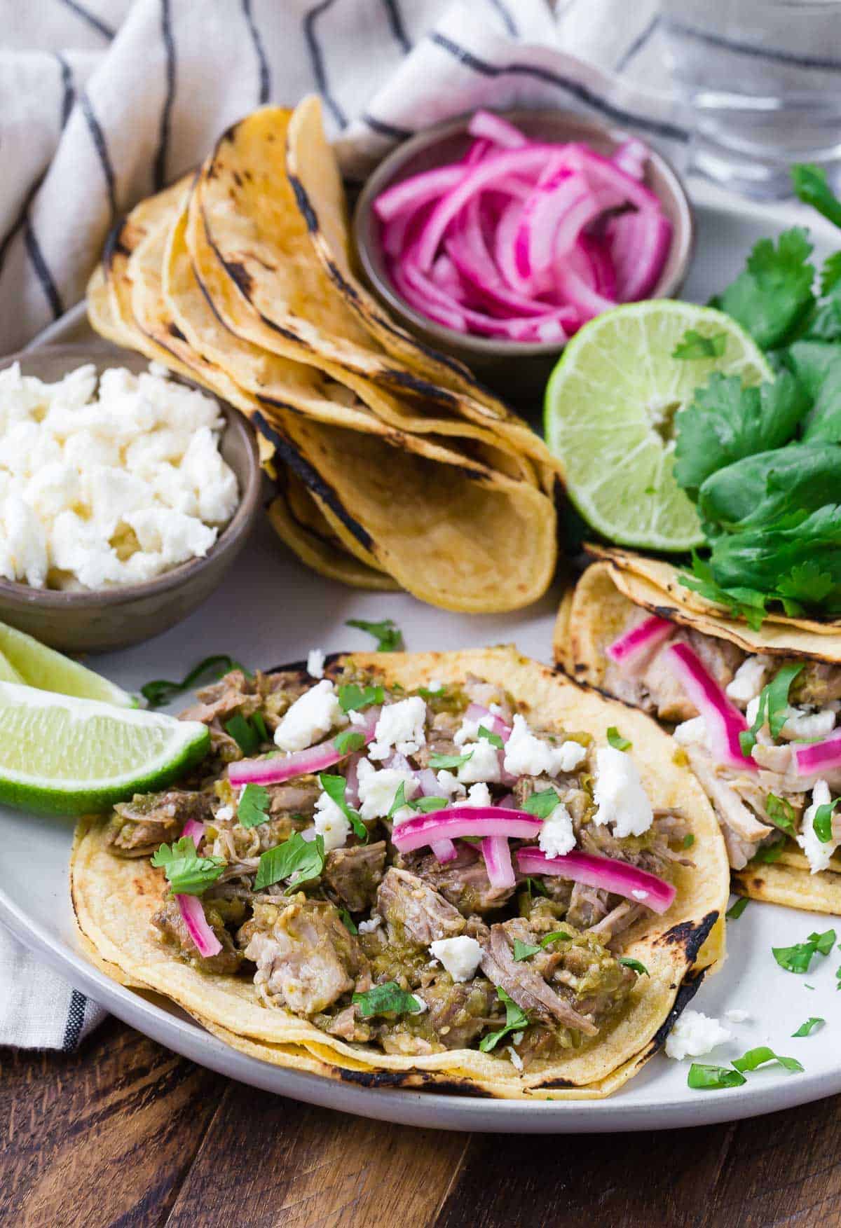 Pork verde tacos on a round platter with toppings and additional tortillas.