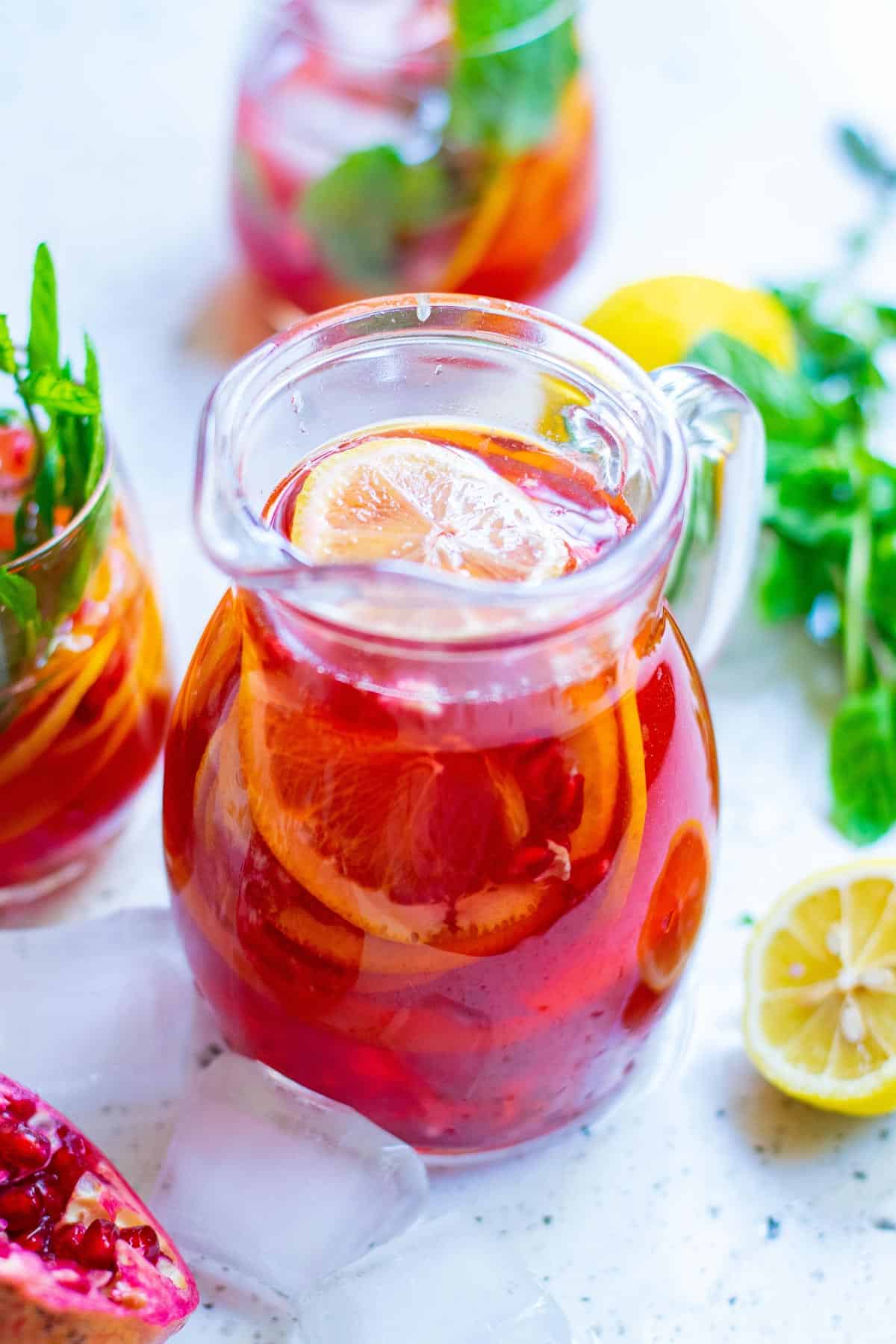 Pitcher of red punch with colorful fresh garnishes.