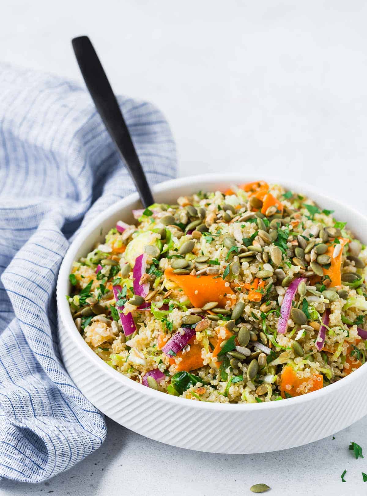 Hearty quinoa salad in a white bowl with a black spoon.