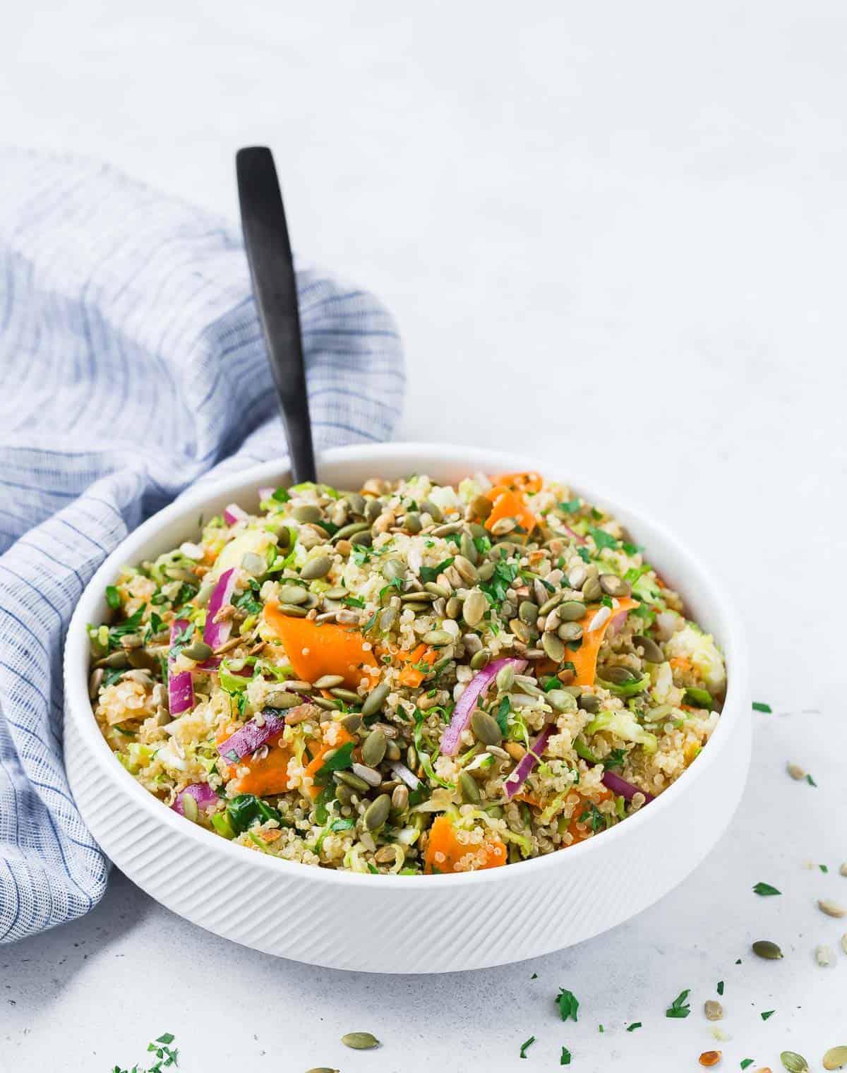 A white bowl filled with colorful salad with quinoa, brussels sprouts, carrots, and red onions.