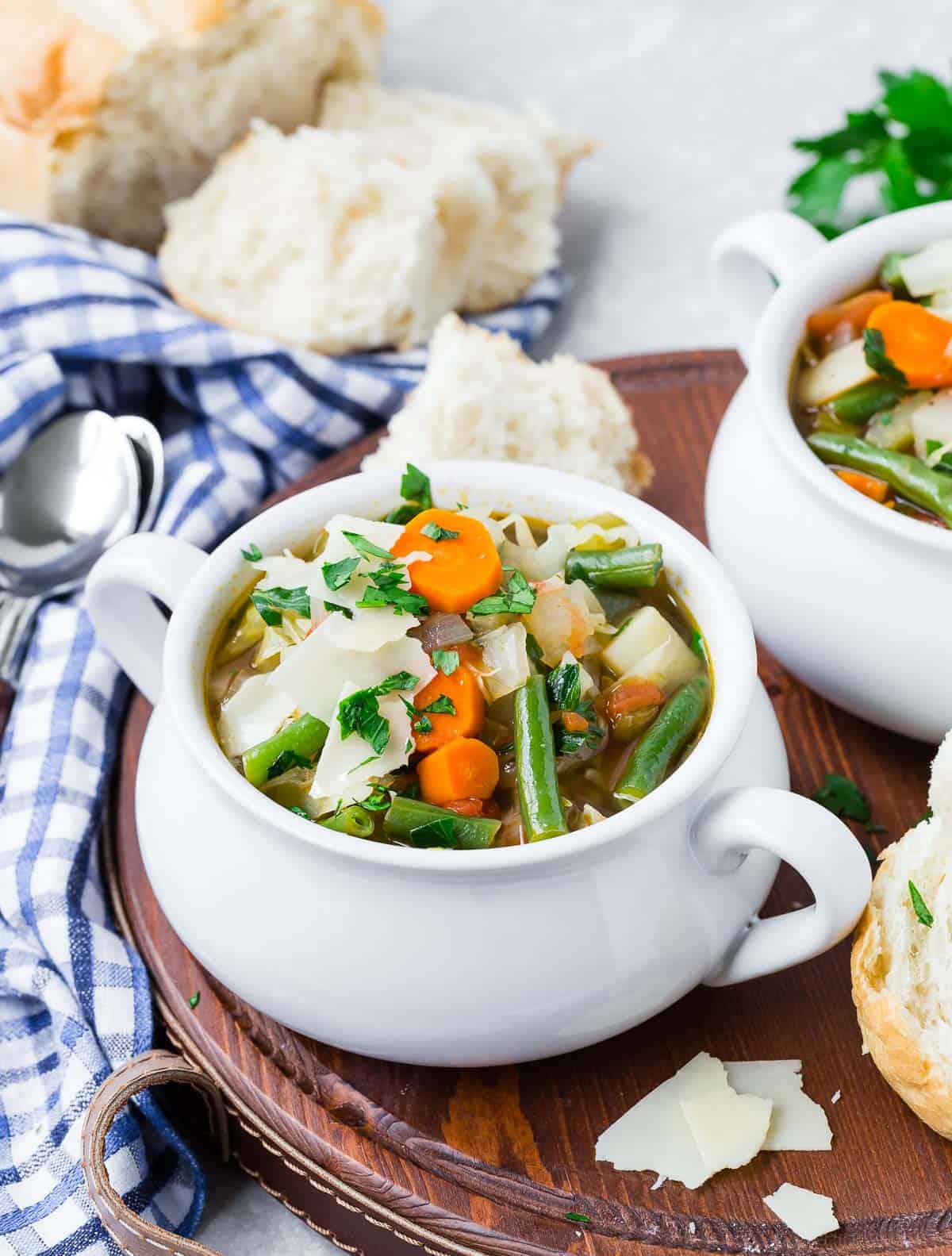 Two bowls of soup on a wooden serving platter with bread.