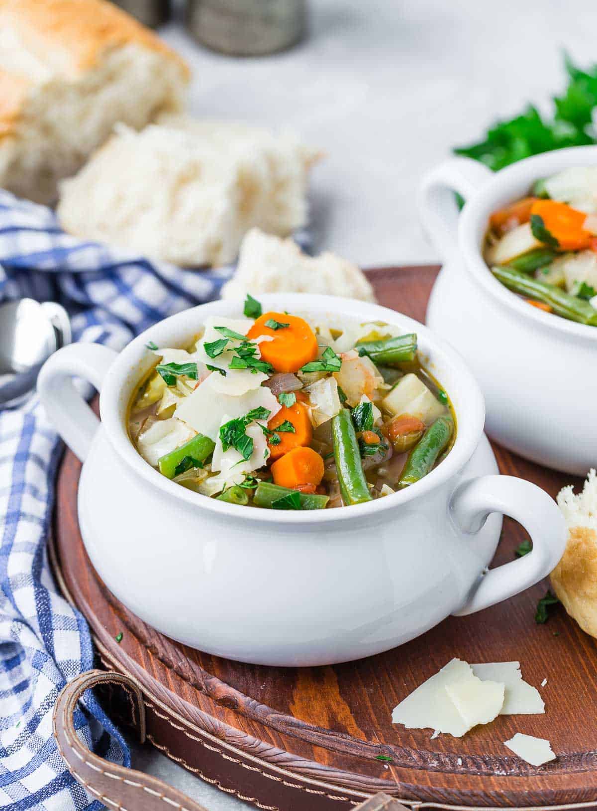 Bowl of soup with vegetables in a small crock style bowl, bread in background.