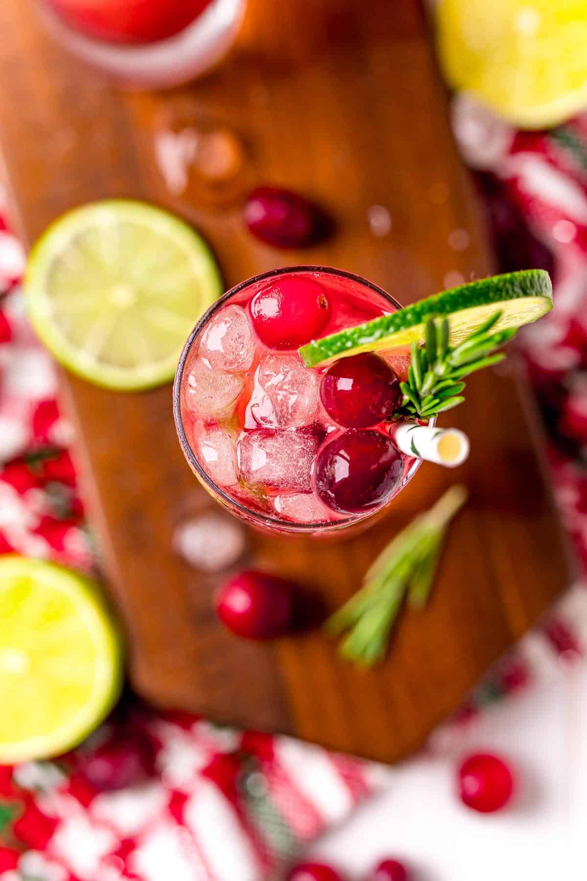 Overhead view of a drink with fresh cranberries, lime slices, and a sprig of rosemary.
