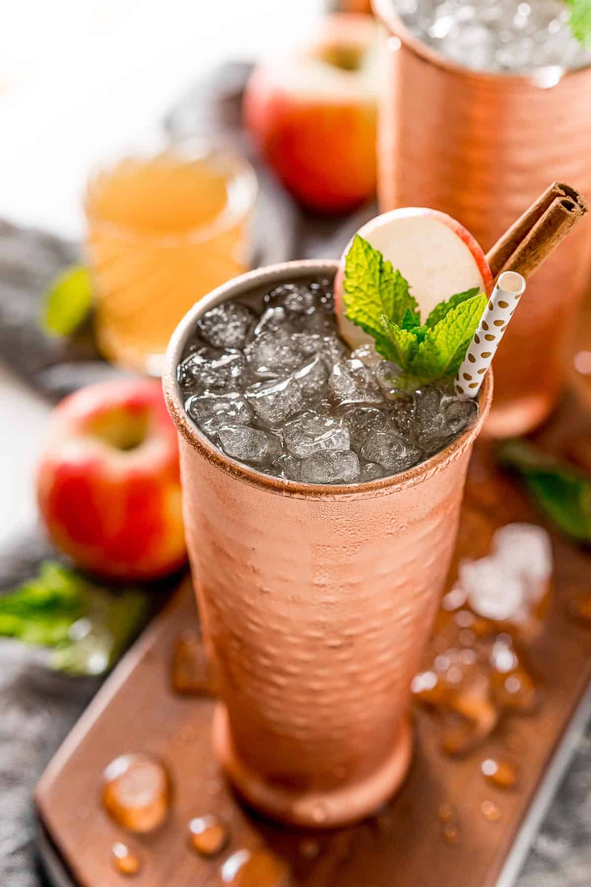 Apple cider moscow mule with nugget ice, garnished with apple, mint leaves, and a cinnamon stick.