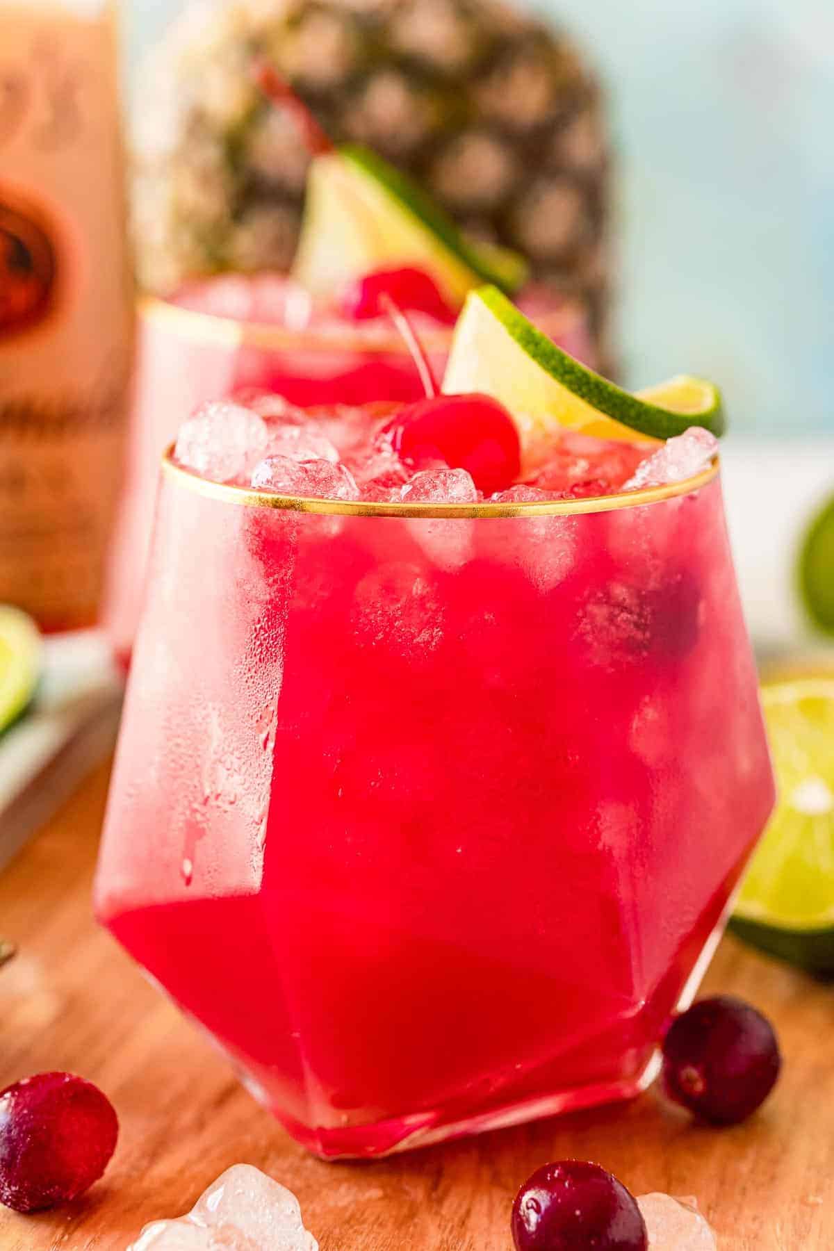 Close up of a bay breeze cocktail garnished with a lime and a cherry.