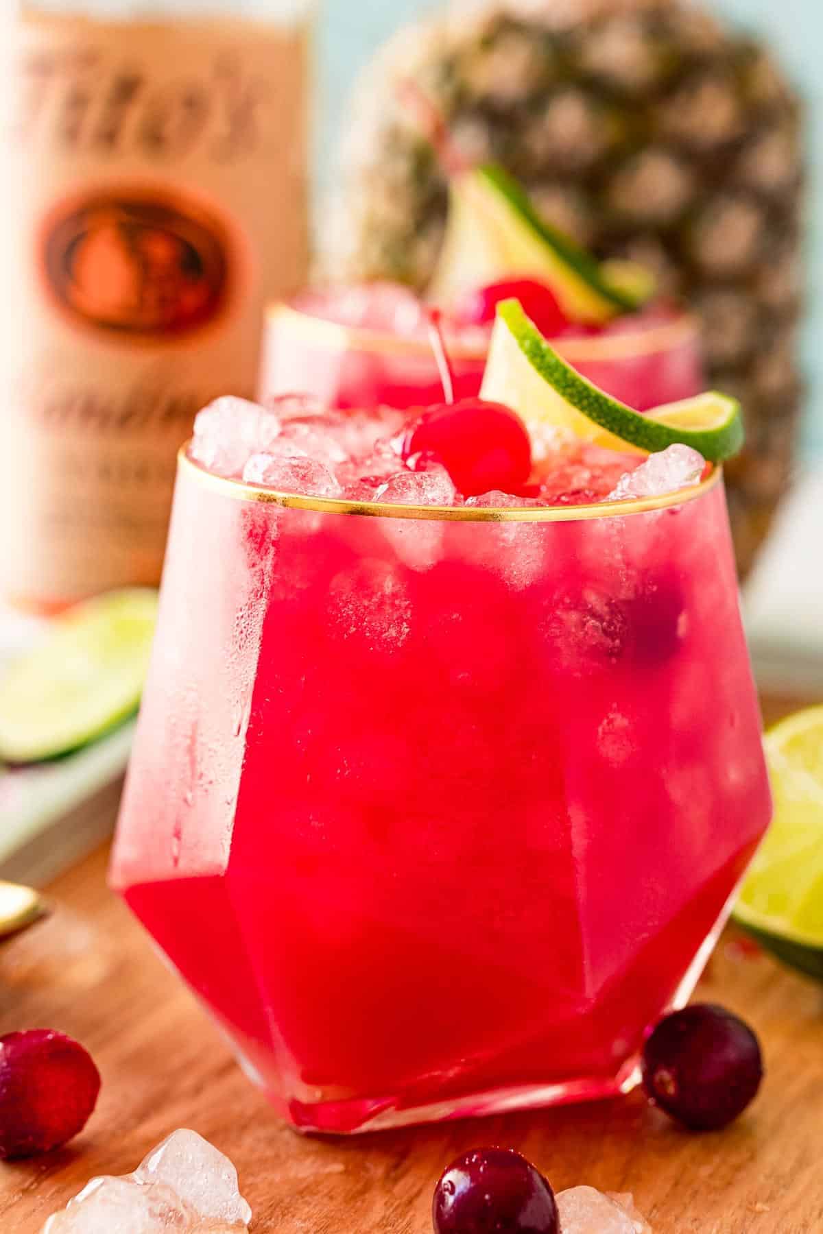 Bright red cocktail with titos and a pineapple in the background.