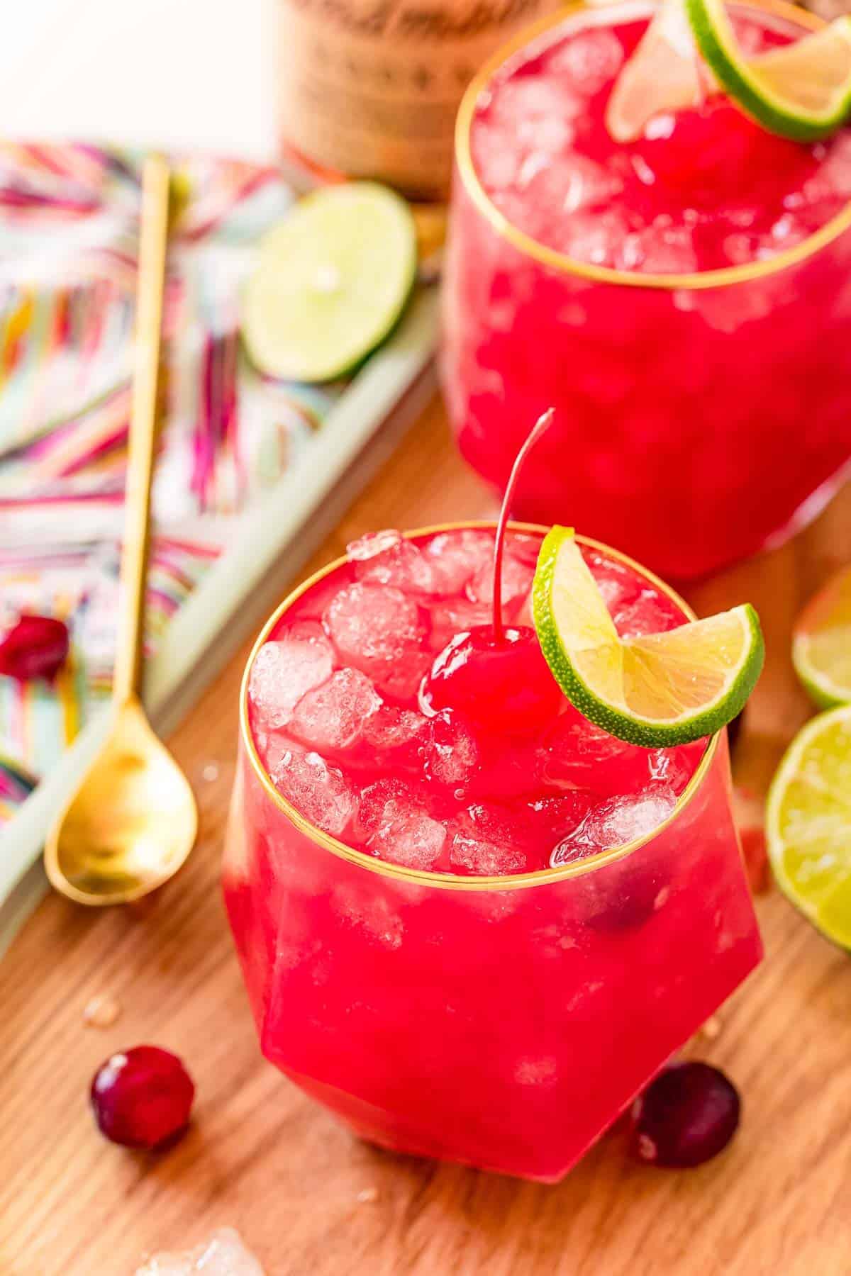 Overhead view of two bright red drinks with ice, a cherry, and a lime. 