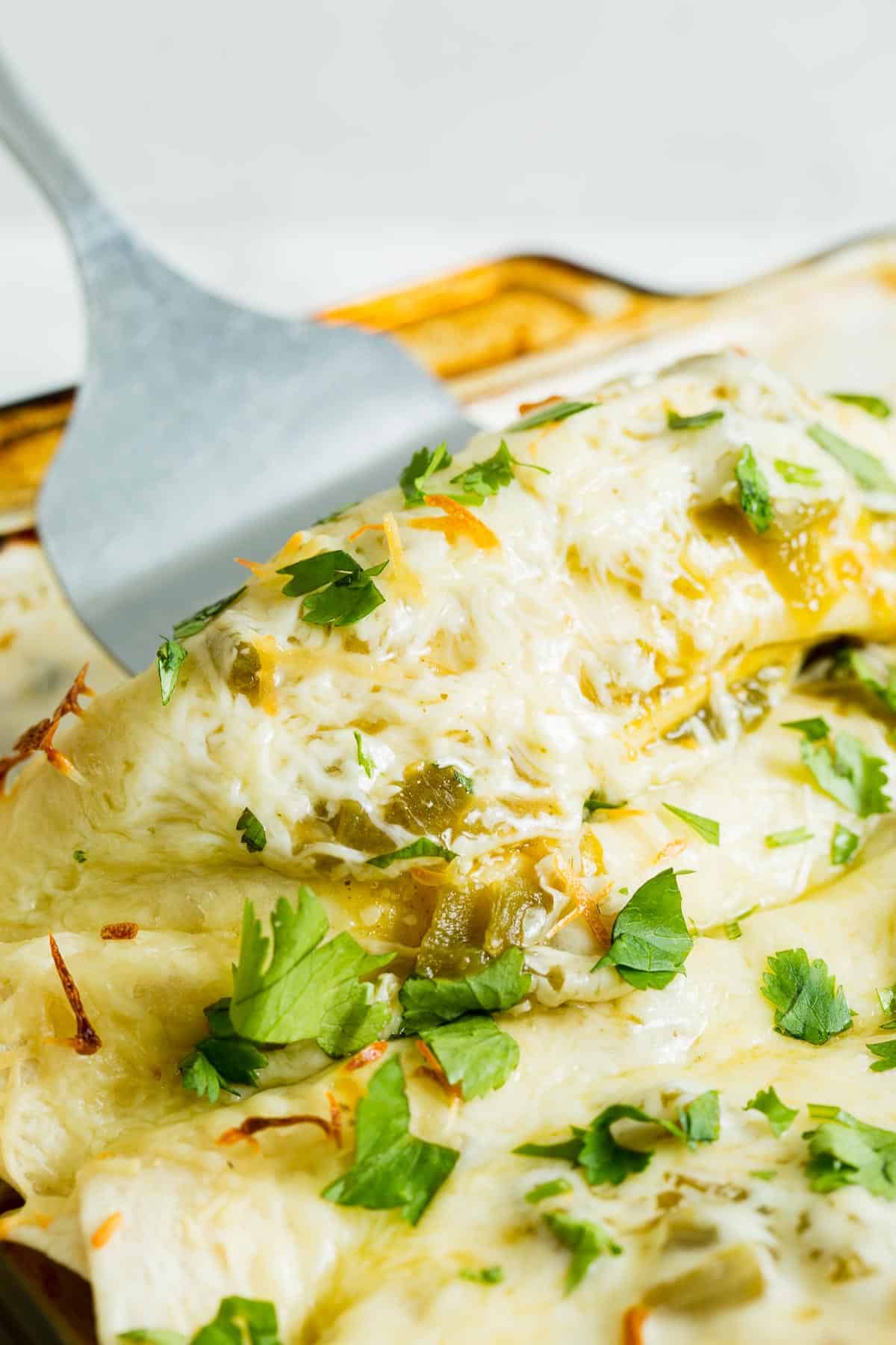 Enchilada being scooped out of a baking dish.