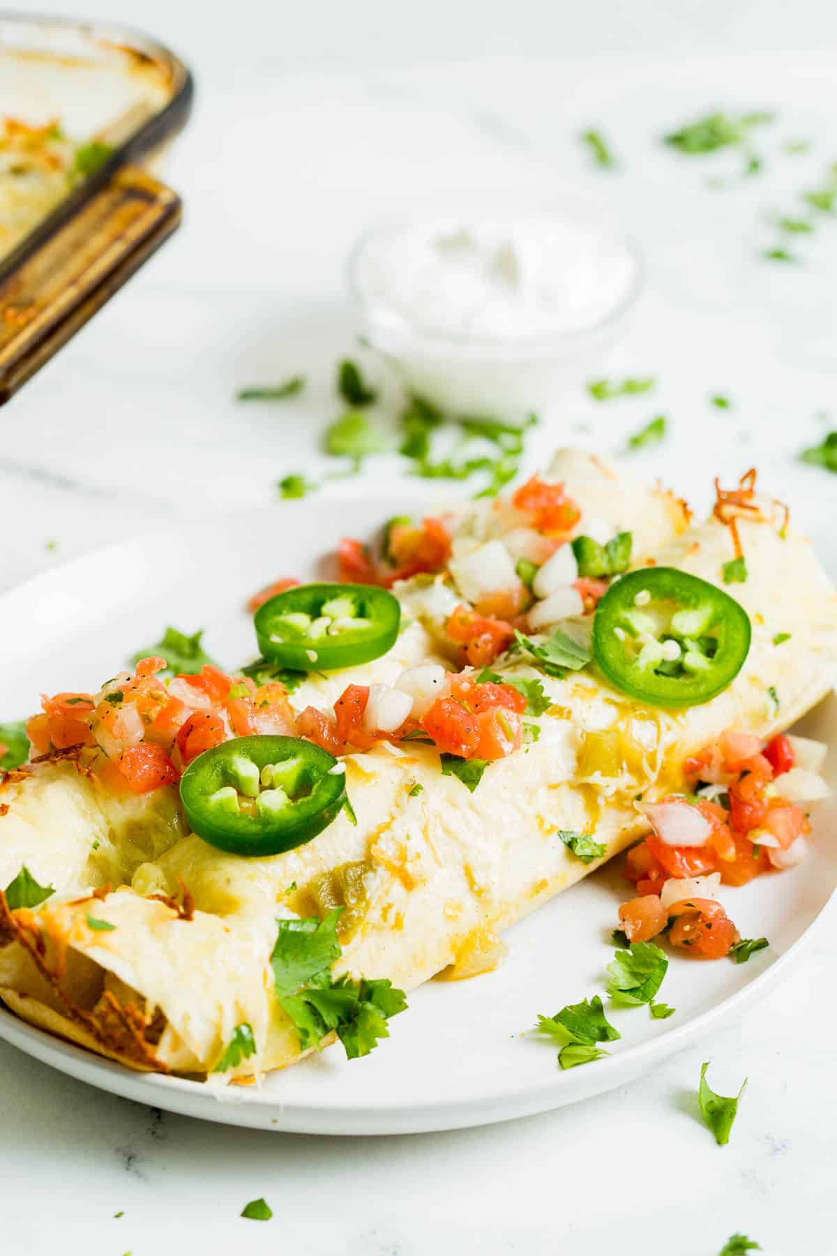 Plated chicken enchiladas verde with jalapeno and cilantro.