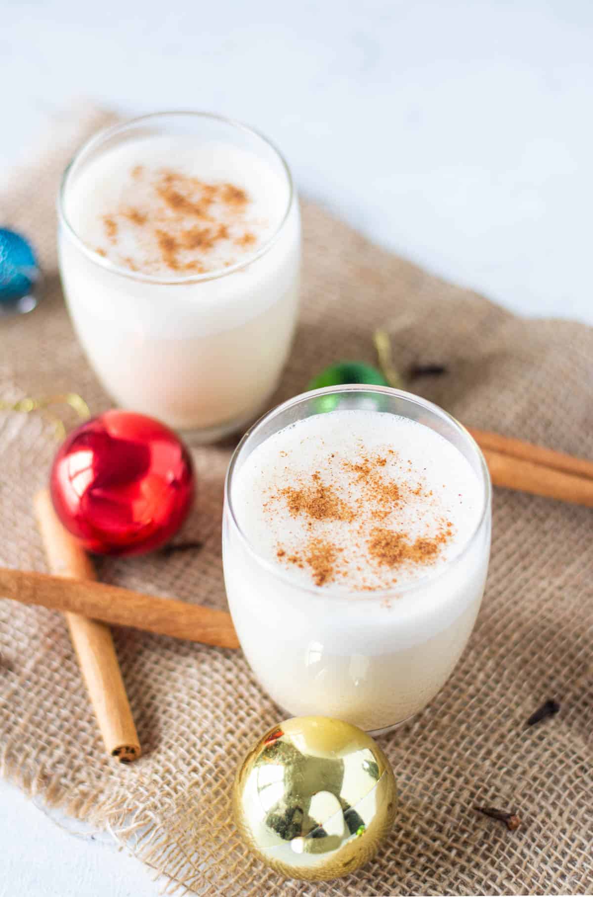 Two glasses of eggnog sprinkled with ground spices.