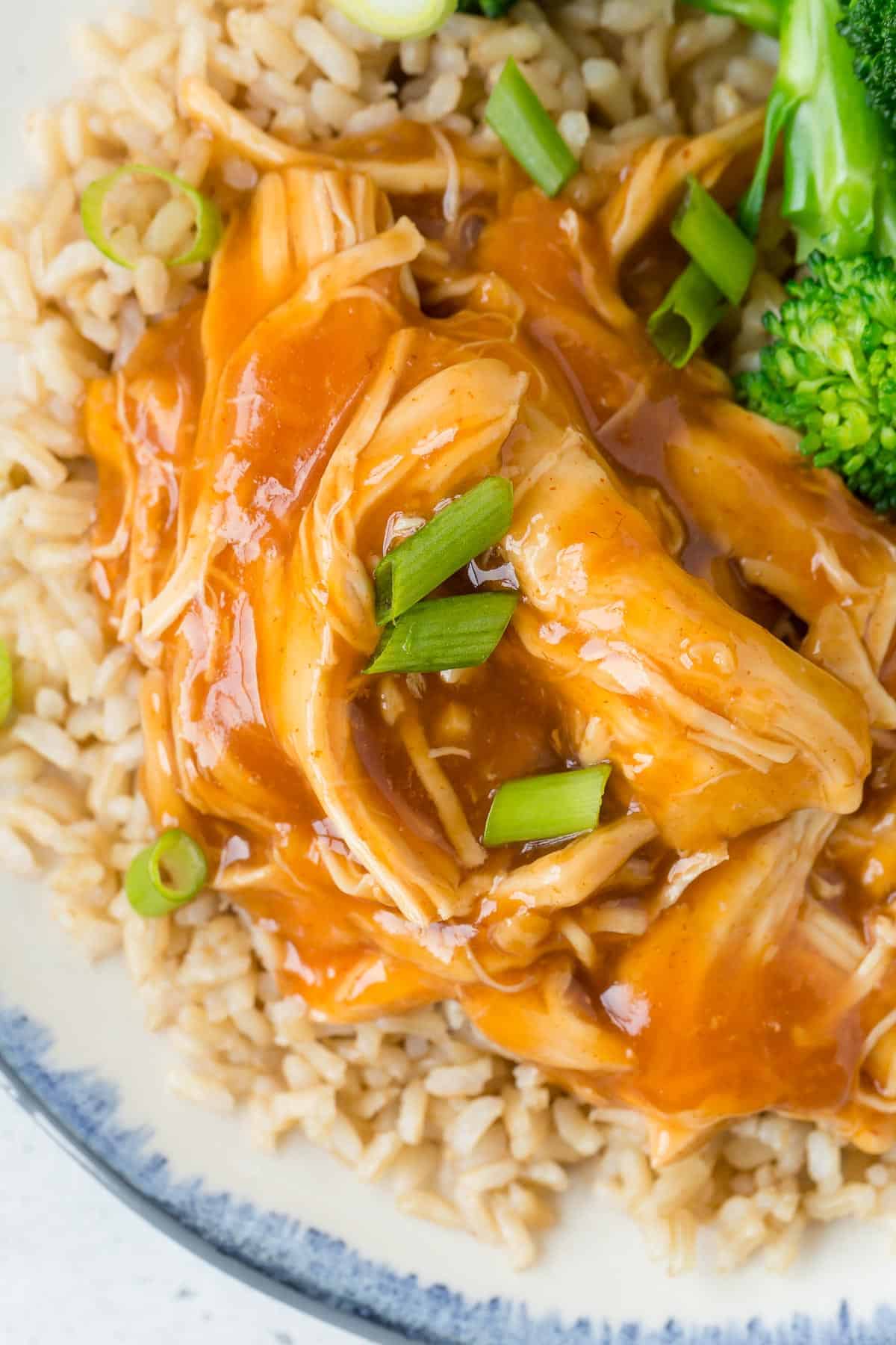 Close up view of pulled chicken with a honey sriracha sauce, served with rice and broccoli.