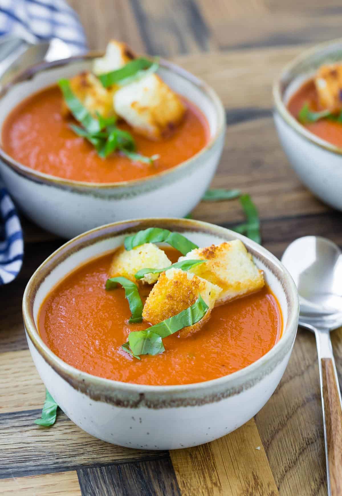 Creamy tomato soup in bowls garnished with croutons and fresh basil.
