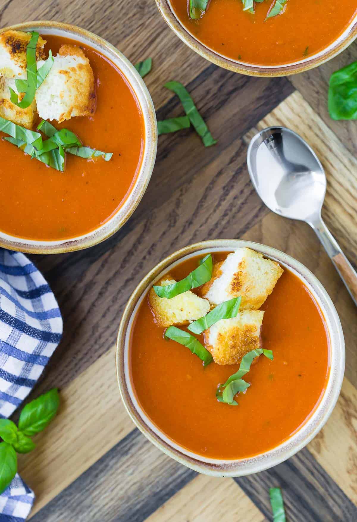 Overhead view of three small bowls of instant pot tomato soup, topped with croutons and fresh basil.