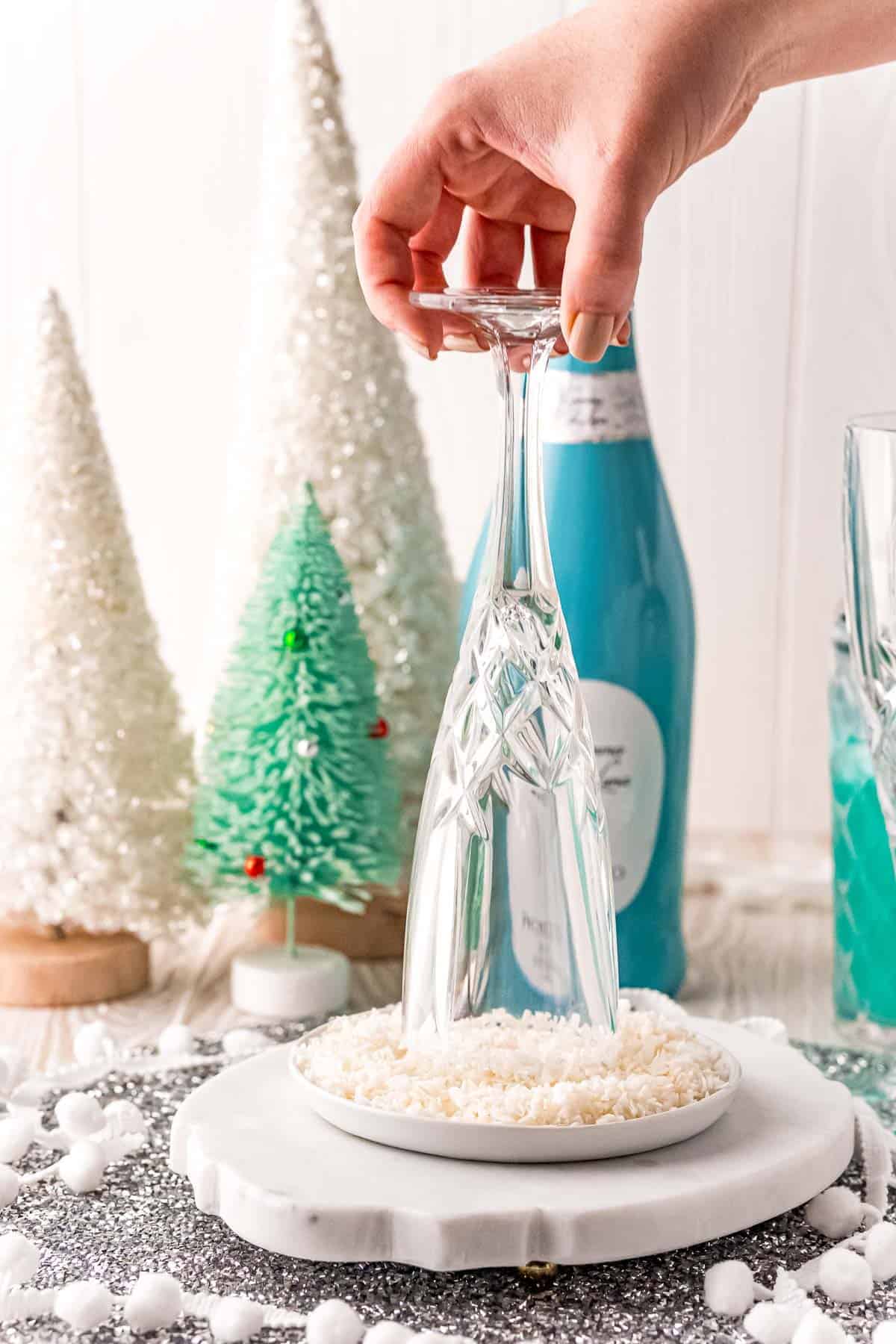 Champagne flute being rimmed with coconut flakes.