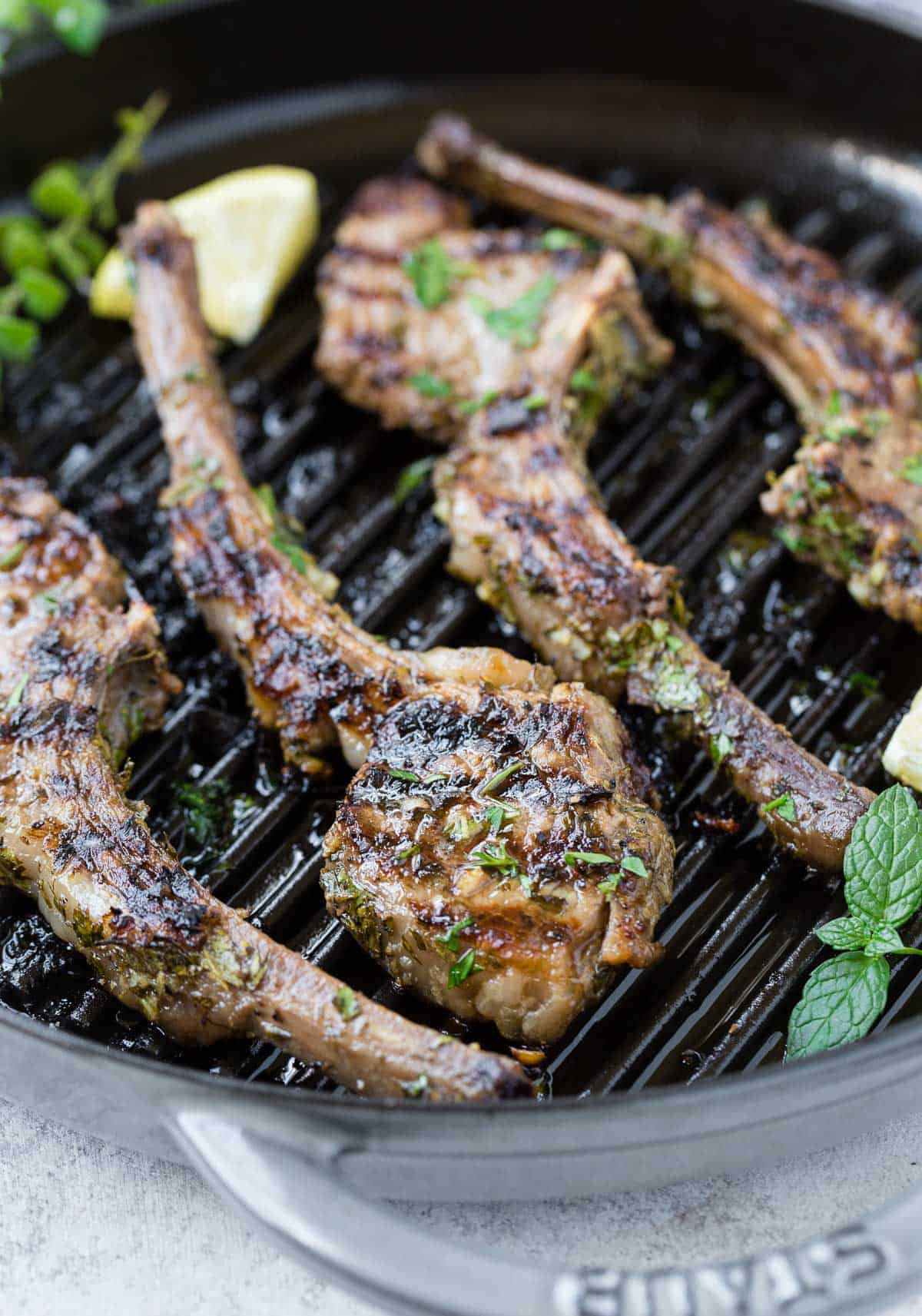 Cooked lamb on a grill pan with fresh herbs and lemon.