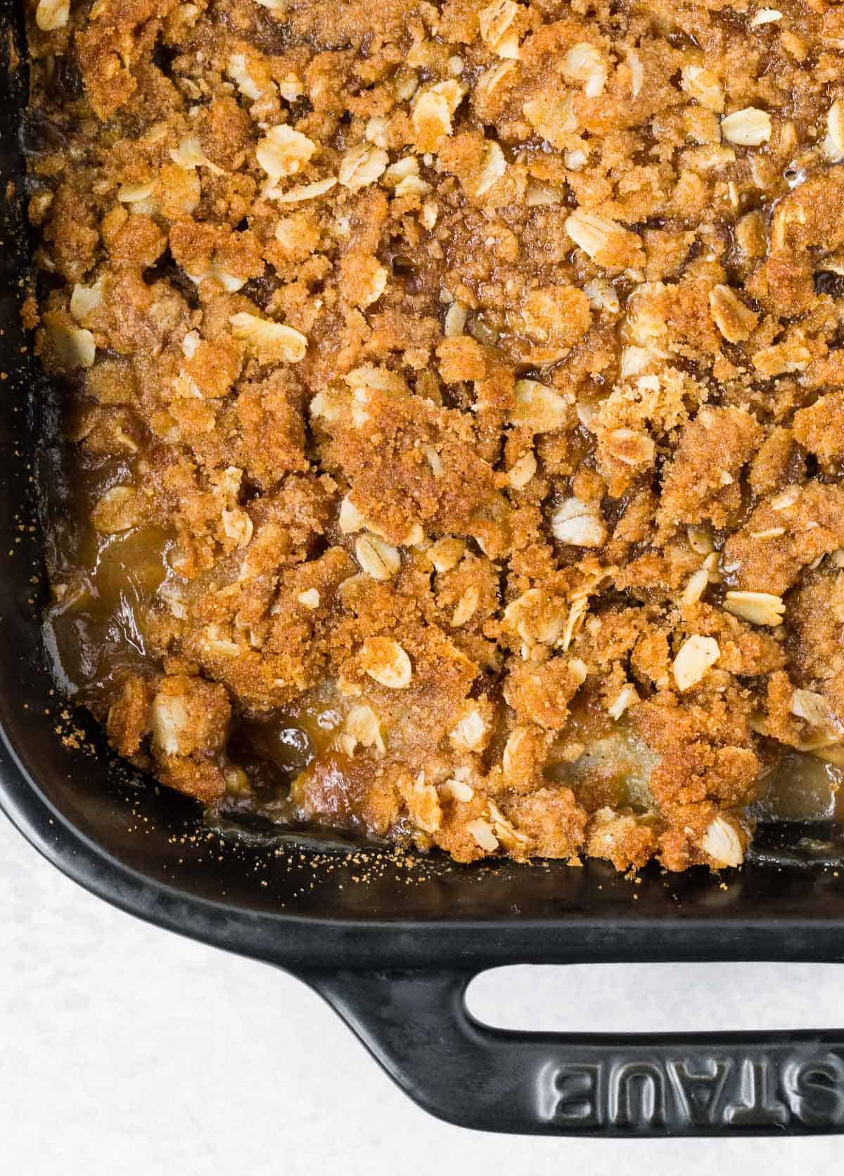 Close up of crisp topping over baked fruit in a black baking dish.