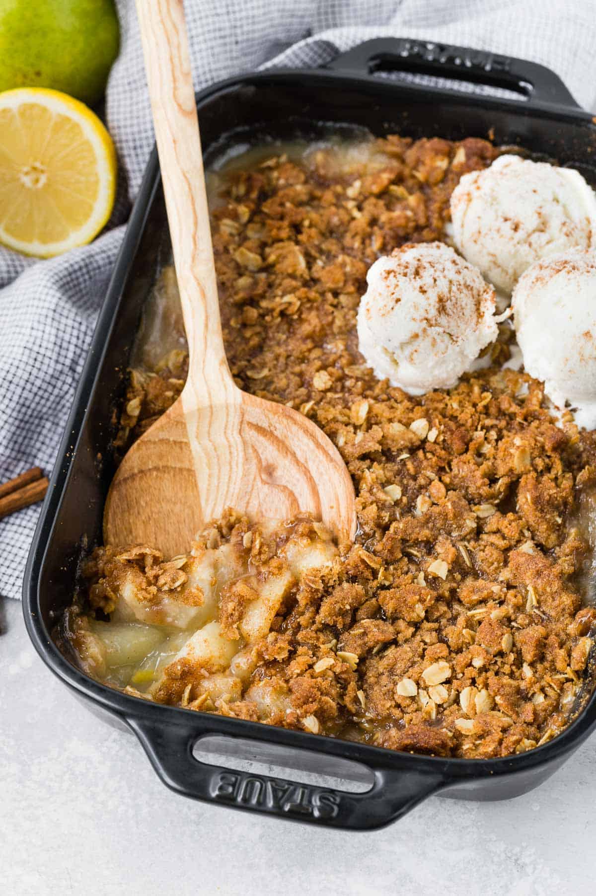 Black baking dish with pear crumble spiced with cinnamon and ginger. Topped with ice cream.