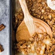 Pear crisp in a black baking dish with a wooden spoon.