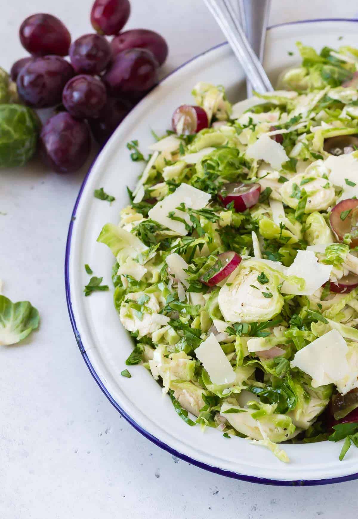 Salad on a blue-rimmed white plate with brussels sprouts and grapes.