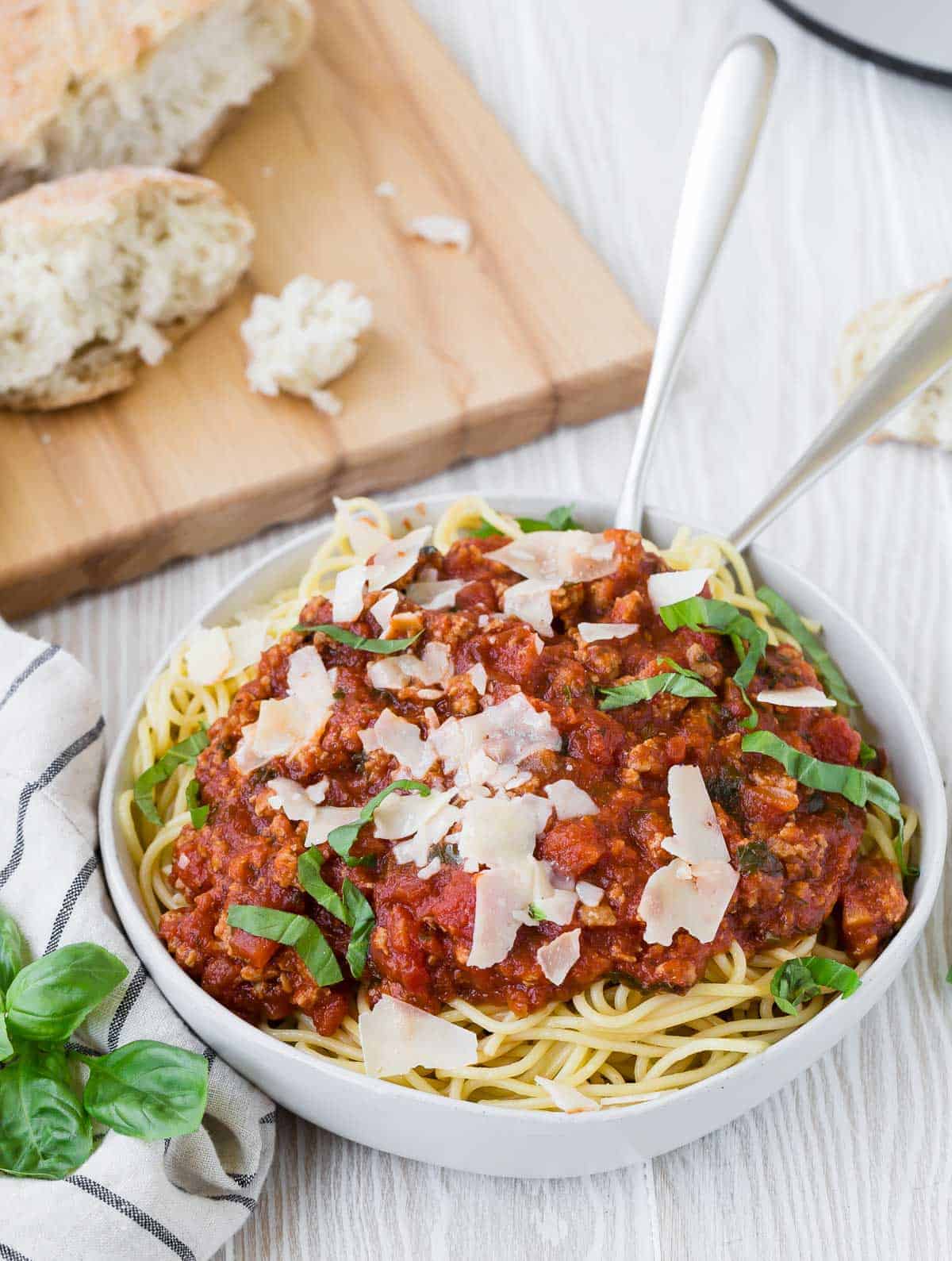 Spaghetti and meat sauce in a white bowl with fresh basil and parmesan garnishes.